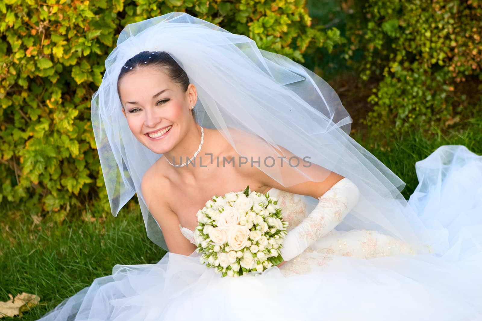 a portrait of the beautiful happy bride under the veil with a flower bouquet in her hands