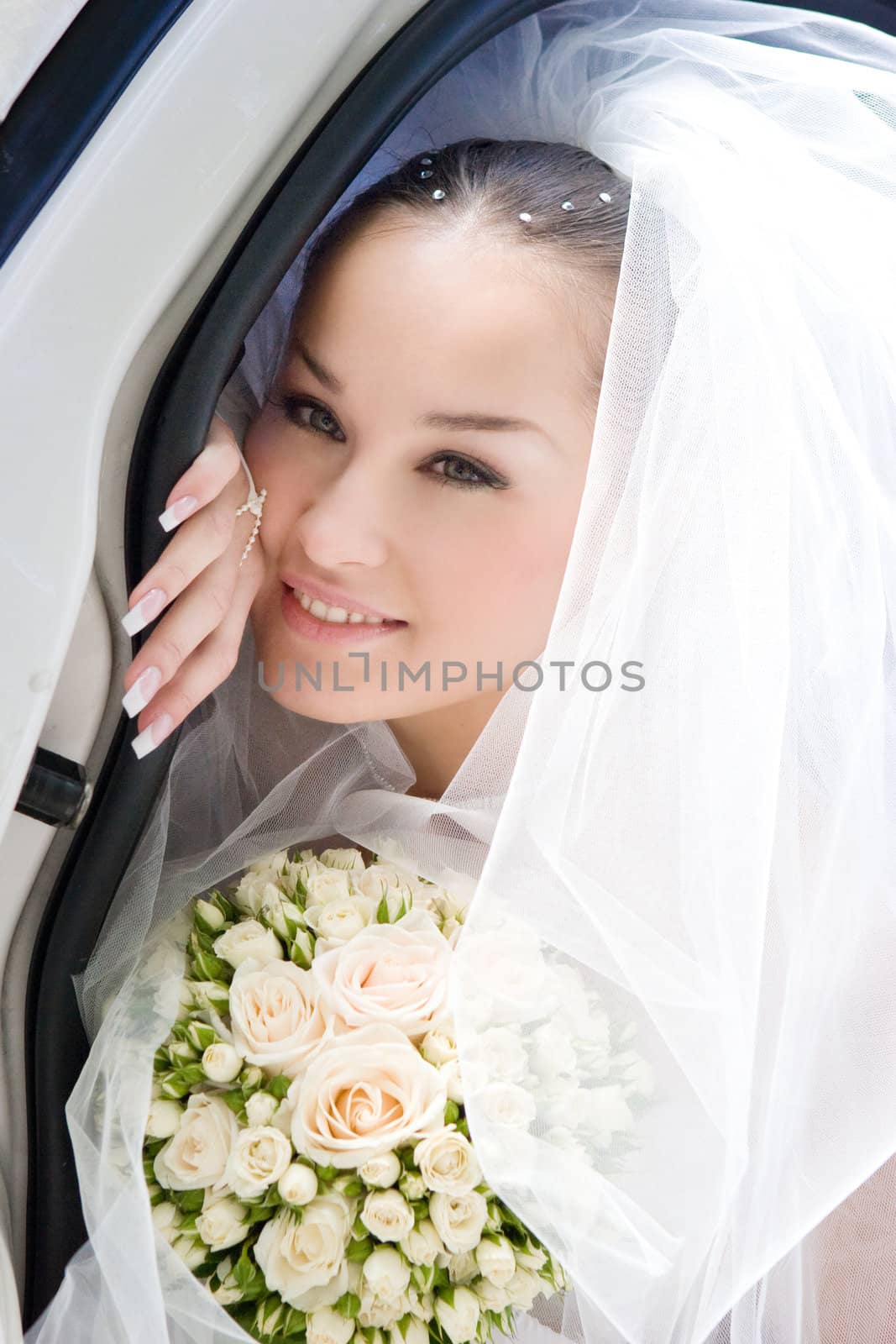 The happy bride with a flower bouquet looks out from the open door of the car