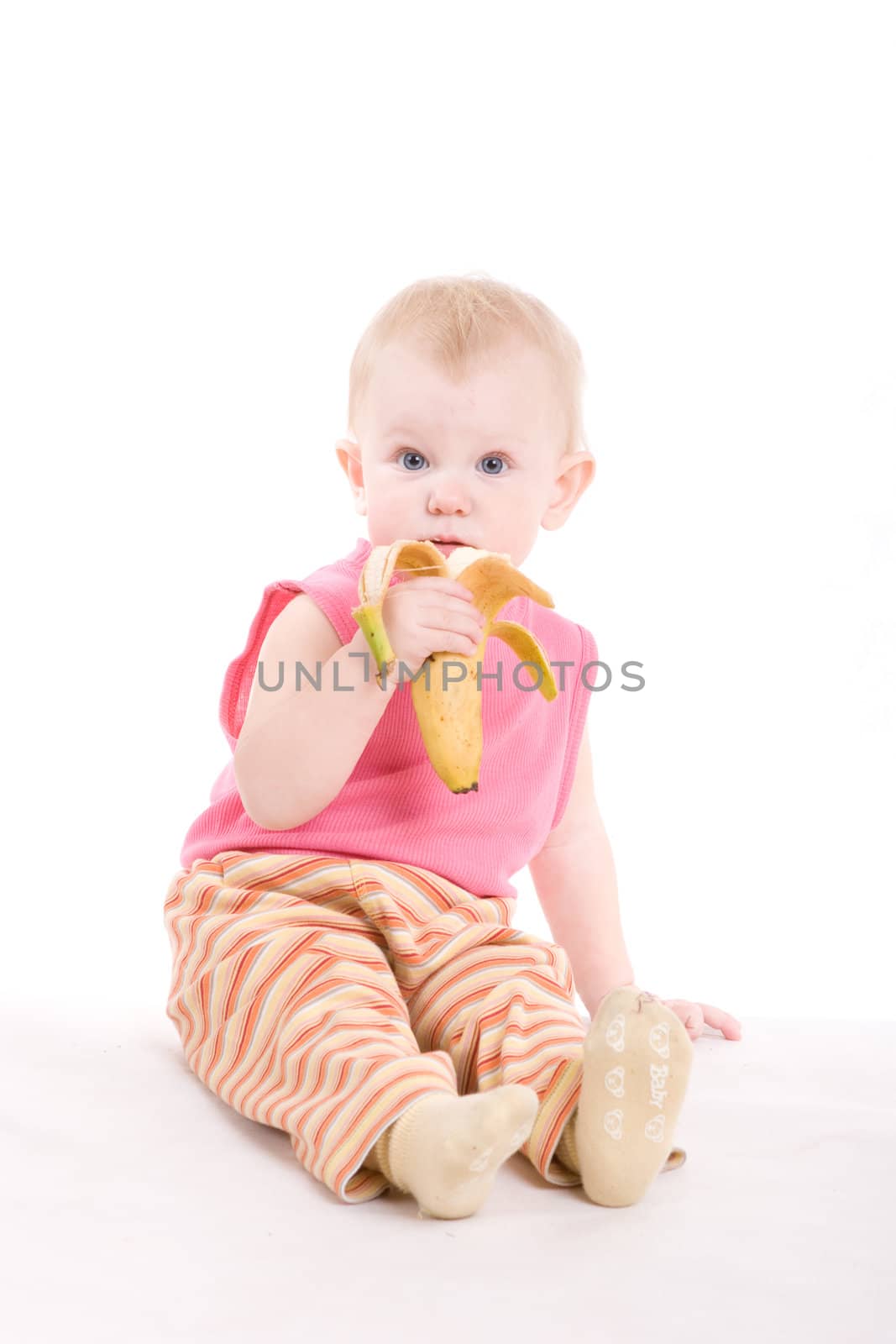 a small surprised girl eating a banana on the floor by vsurkov