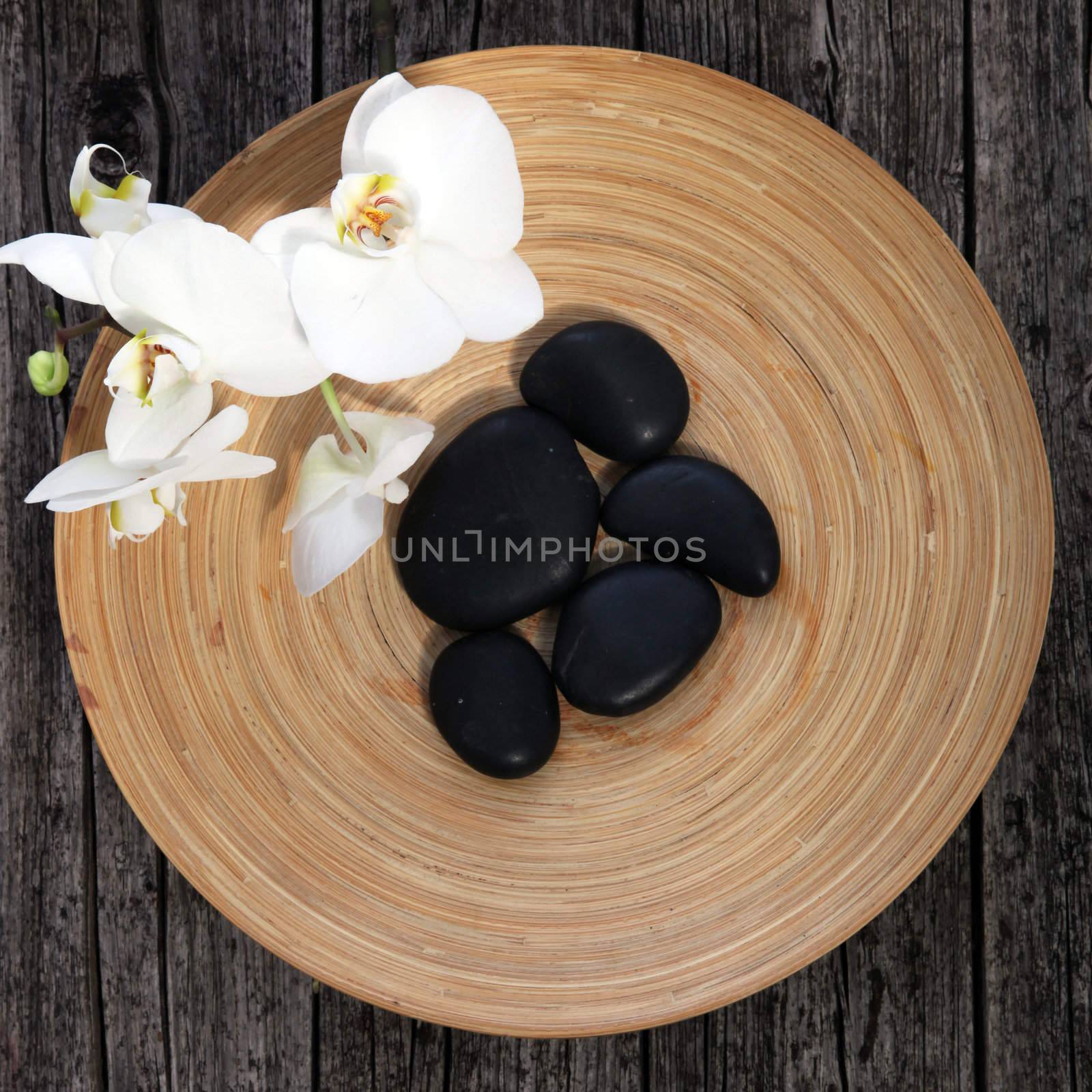 Overhead view of smooth black basalt massage stones in a pottery bowl with integral concentric patterning with fresh white flowers for an unusual spa background