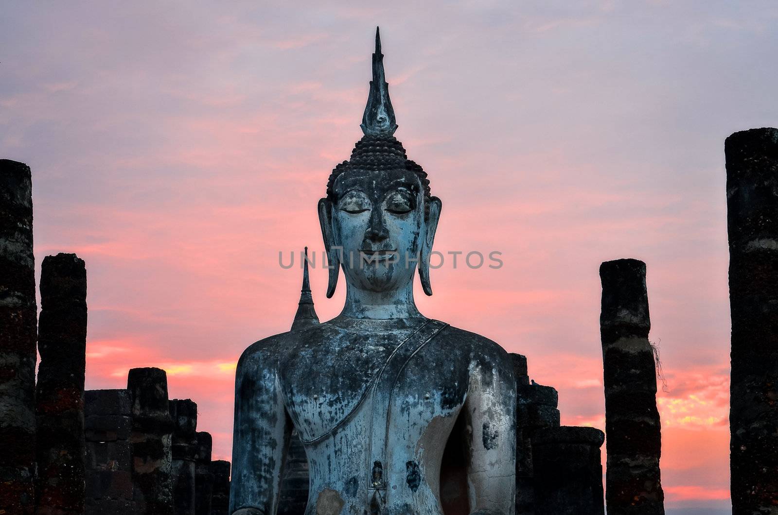 Detail of sitting Buddha at colorful sunset in Sukhothai historical park, Thailand