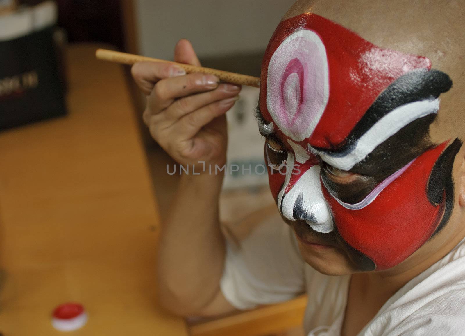 a chinese opera actor is painting his face backstage by jackq