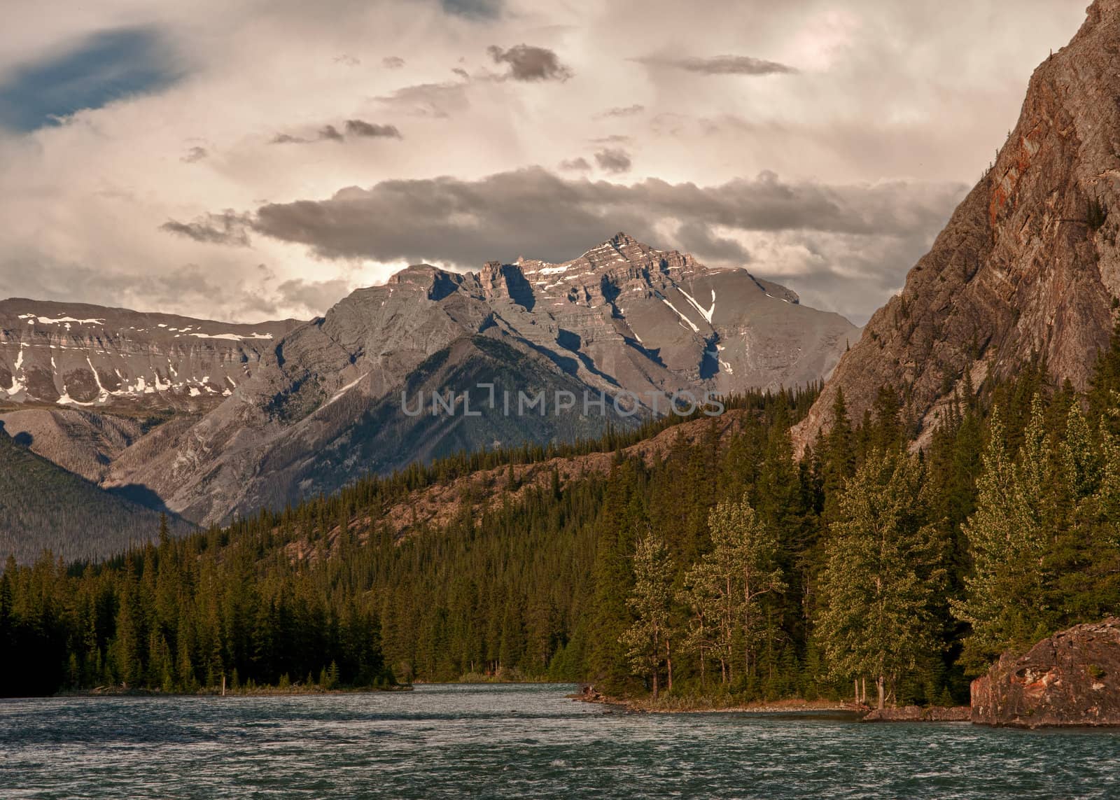 Dark clouds are moving in during sunset on the river near Banff  by Claudine