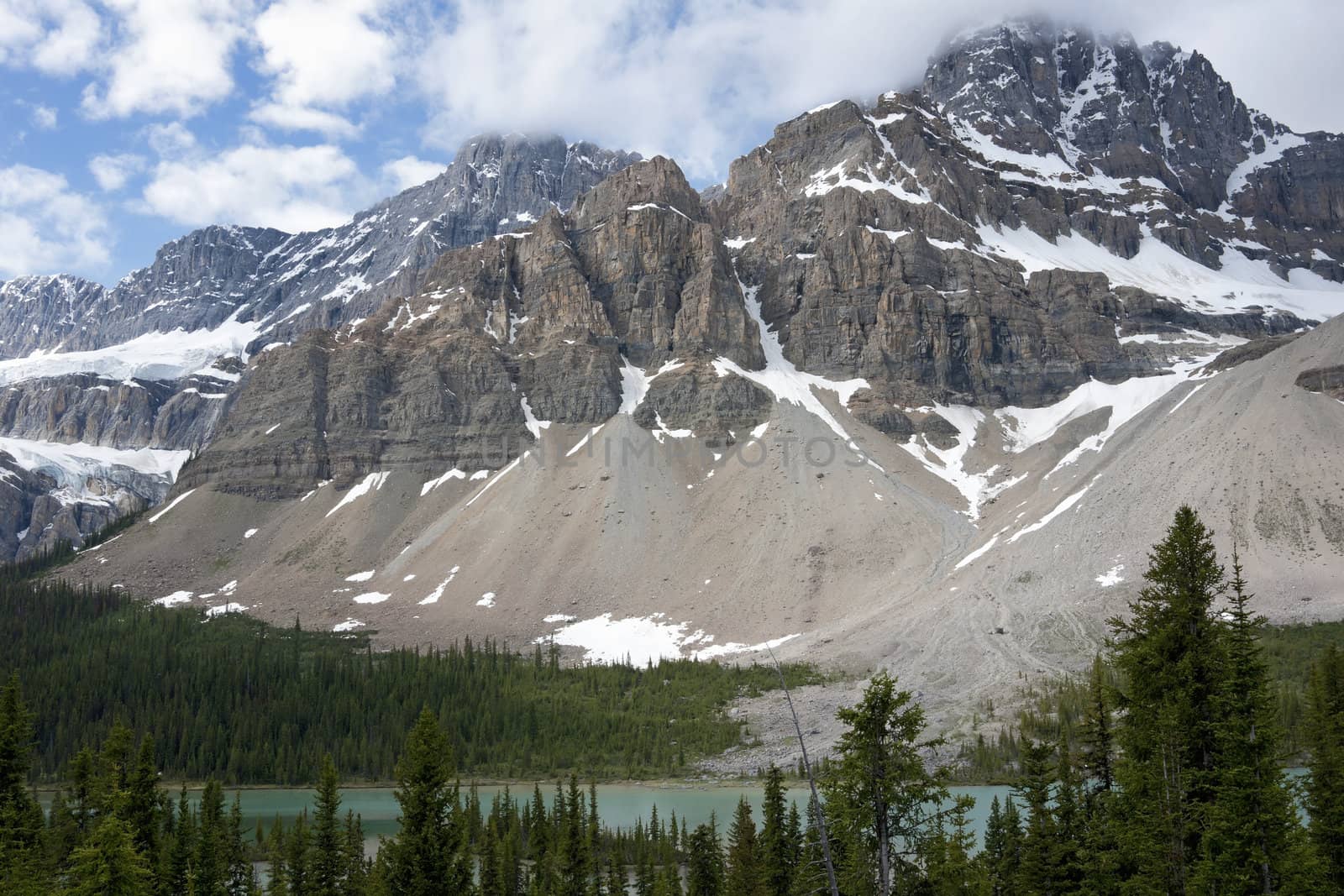Peyto Lake in Alberta (Canada) surrounded by forests lies under towering snow capped mountains. by Claudine