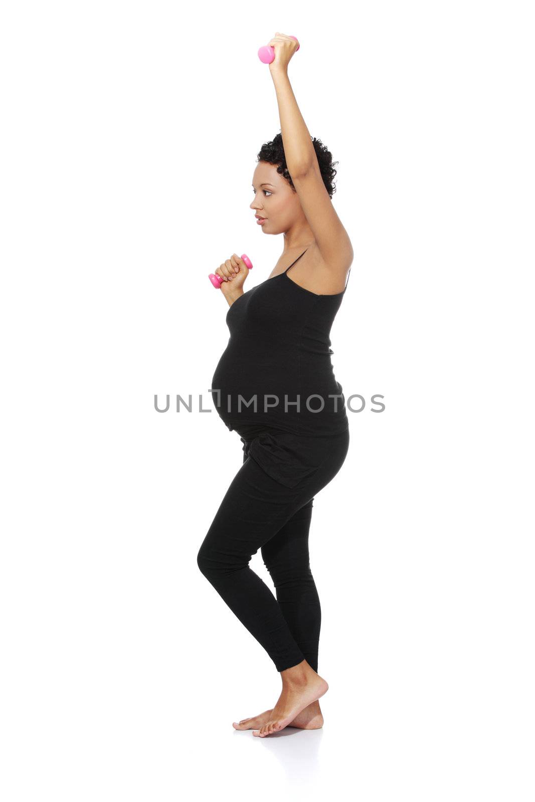 Full lenght site view of a young smiling pregnant woman doing exercises with small weights, isolated on a white background.