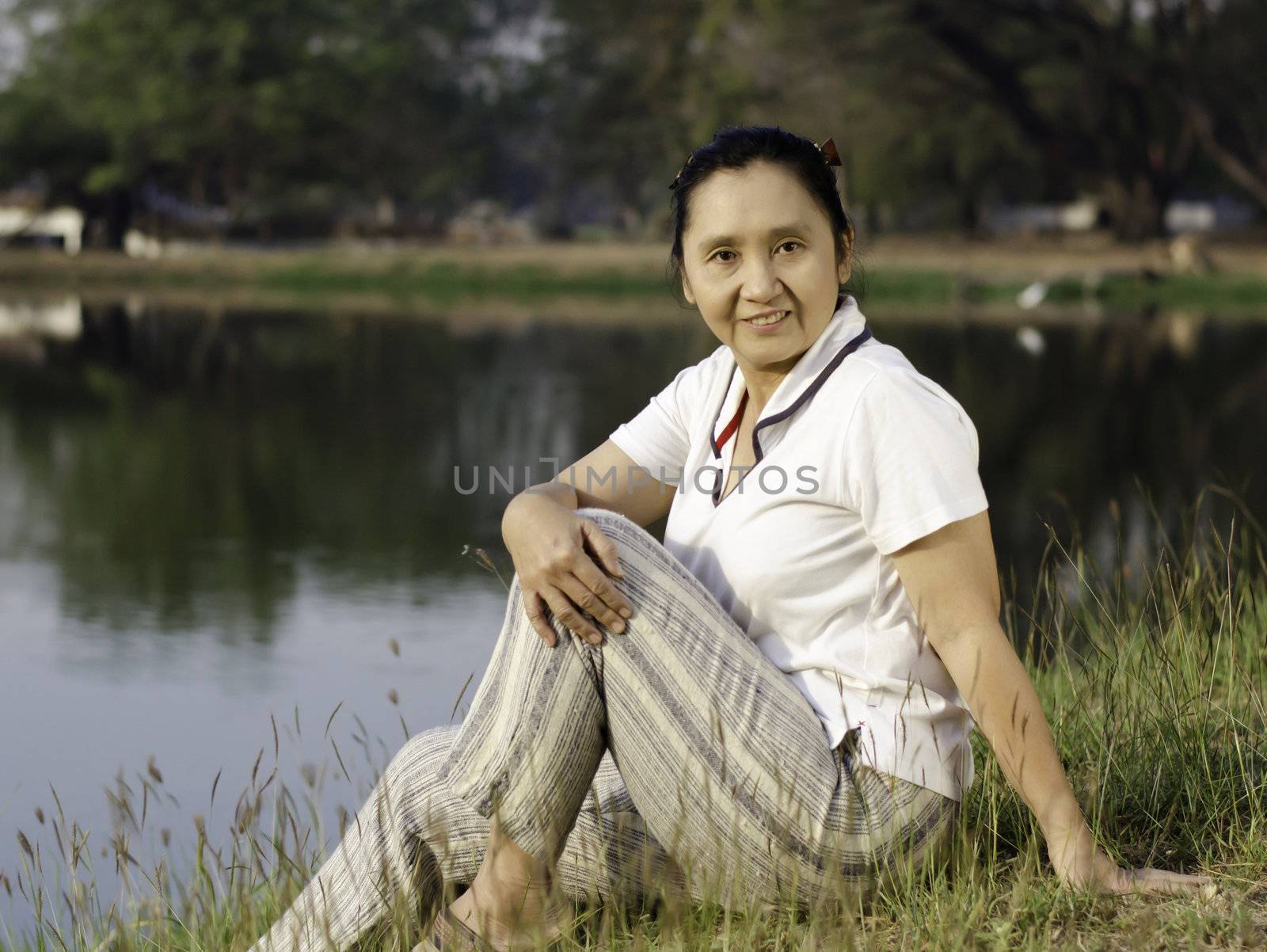 Woman sitting on background of green field by lake