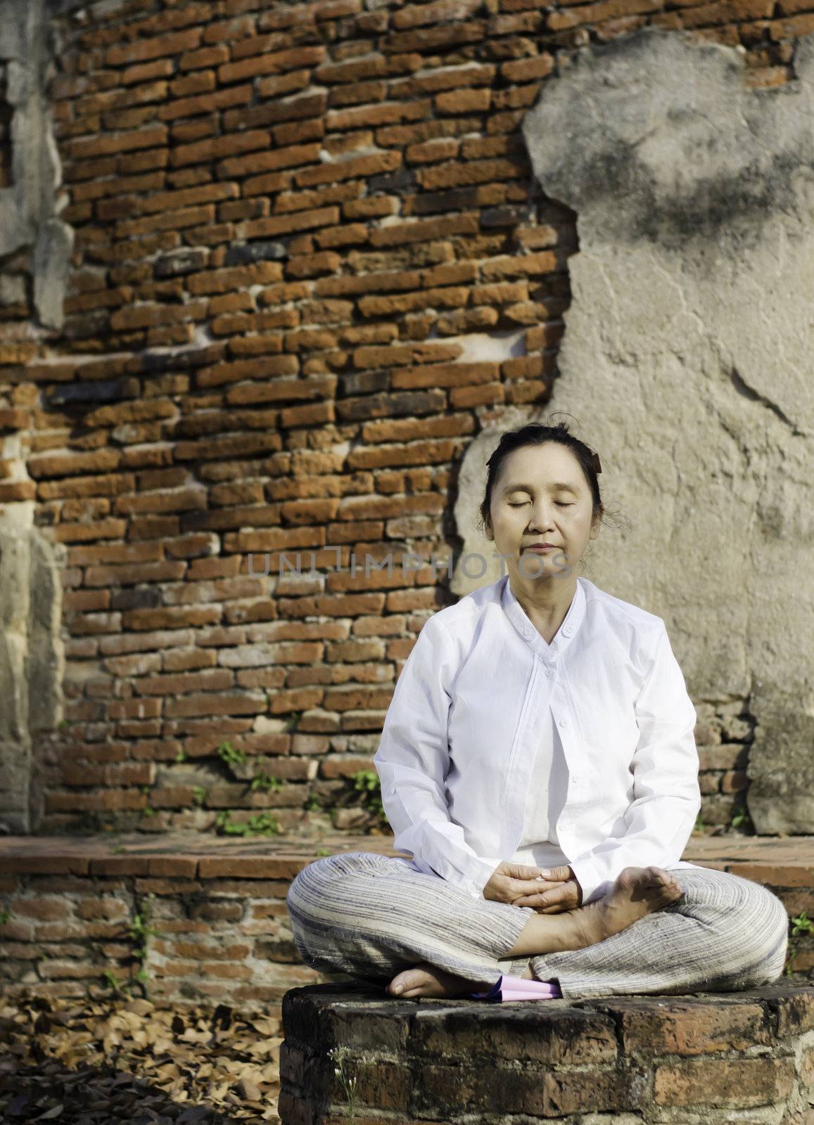 Buddhist woman meditating against ancient temple