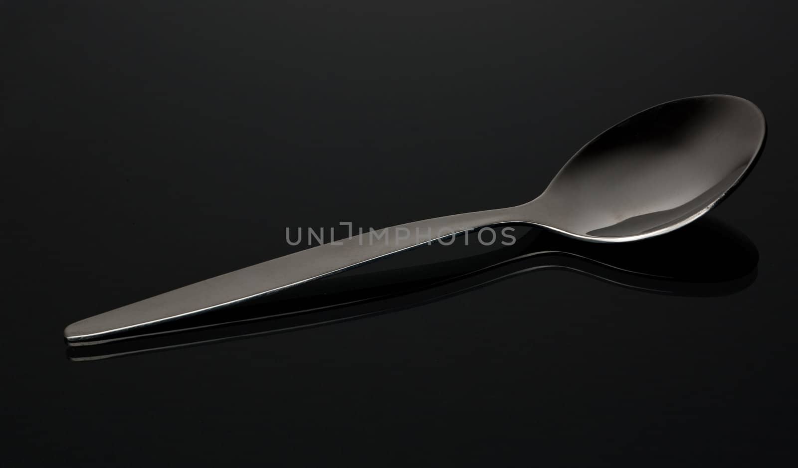 empty shiny silver spoon  on black reflective surface