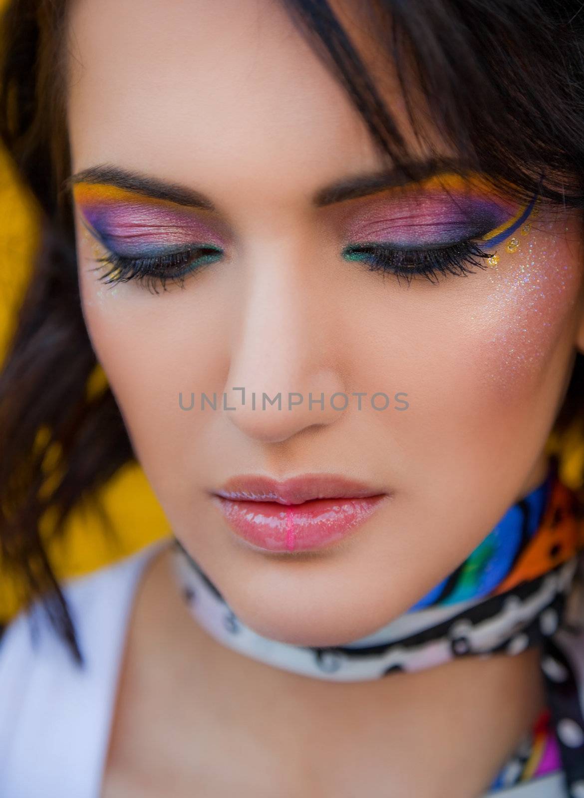 Portrait of beautiful young female with fancy colourful makeup, looking down