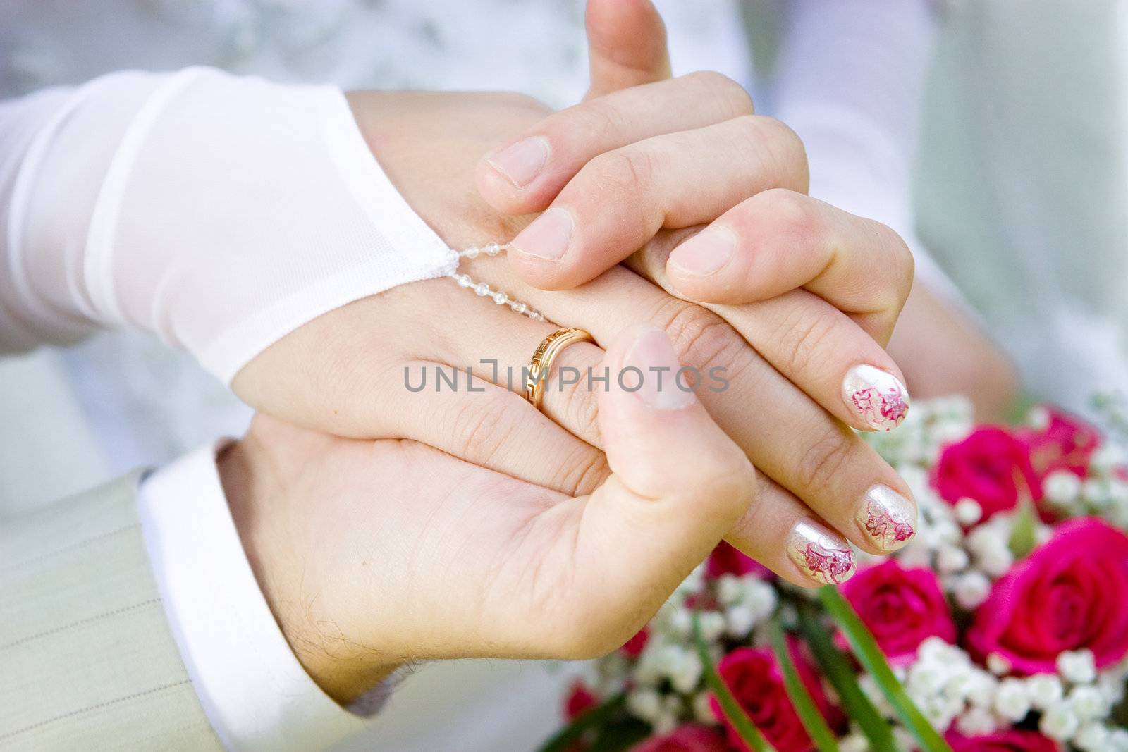 a hand of a groom holds a hand of a bride with a wedding ring on