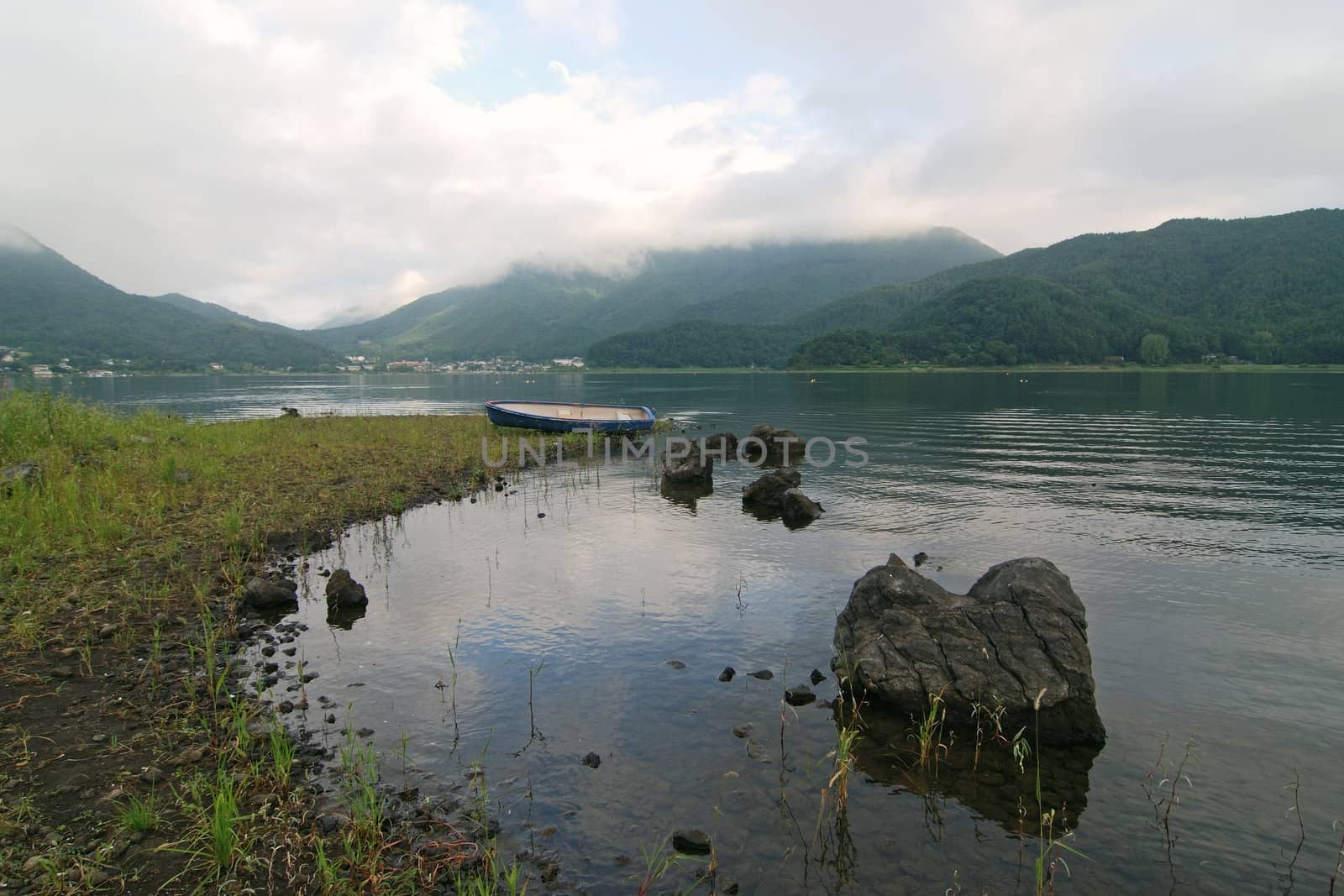 mountain landscape with lake, boulders in water and blue boat backward, Lake Kawaguchi, Japan