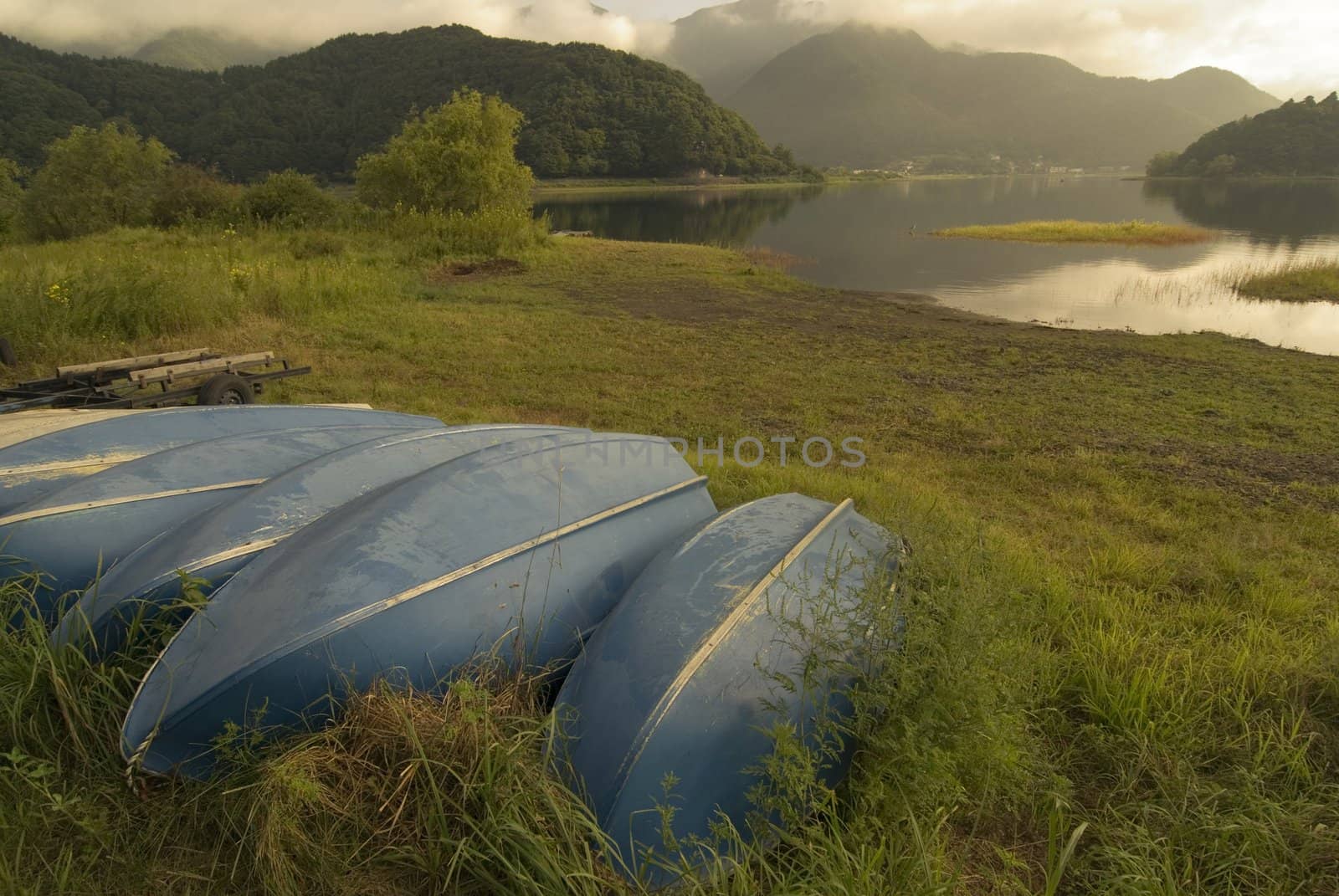 moody summer landscape with blue boats on the grass close to mountain lake, Lake Kawaguchi, Japan