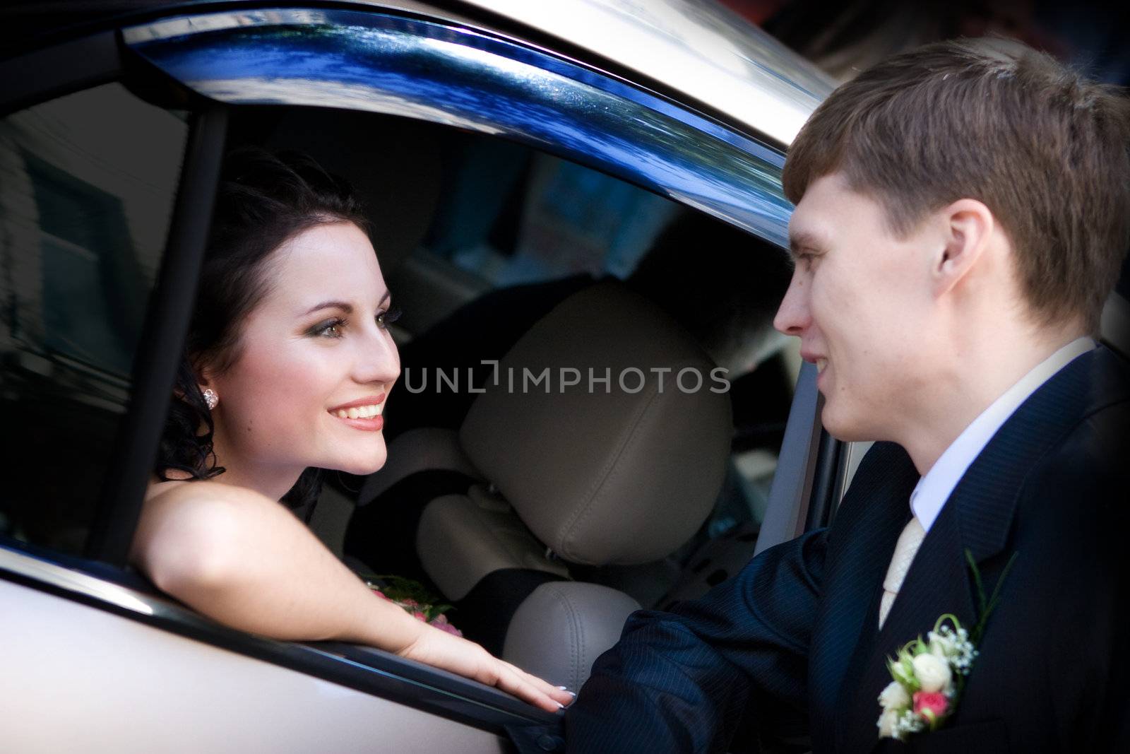 happy bride looks at the groom from the car