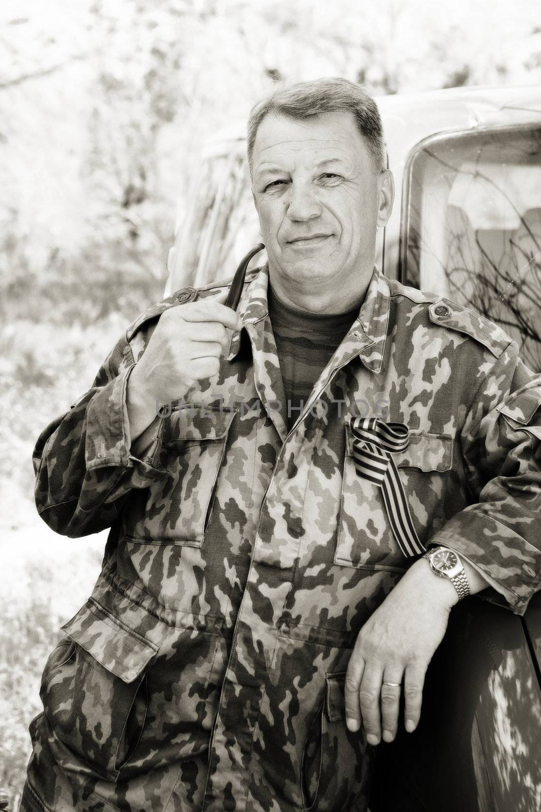 man dressed in camouflage wear smokes pipe in black and white