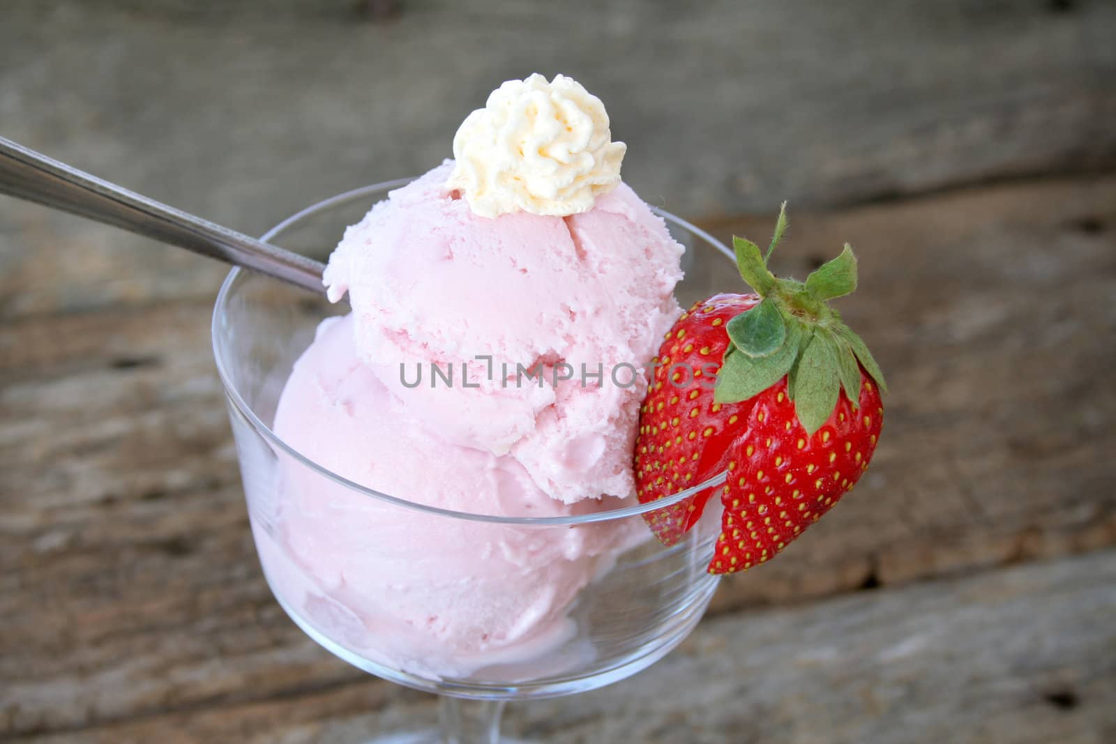 Dish of strawberry ice-cream with a fresh strawberry on the side and topped off with whip cream.