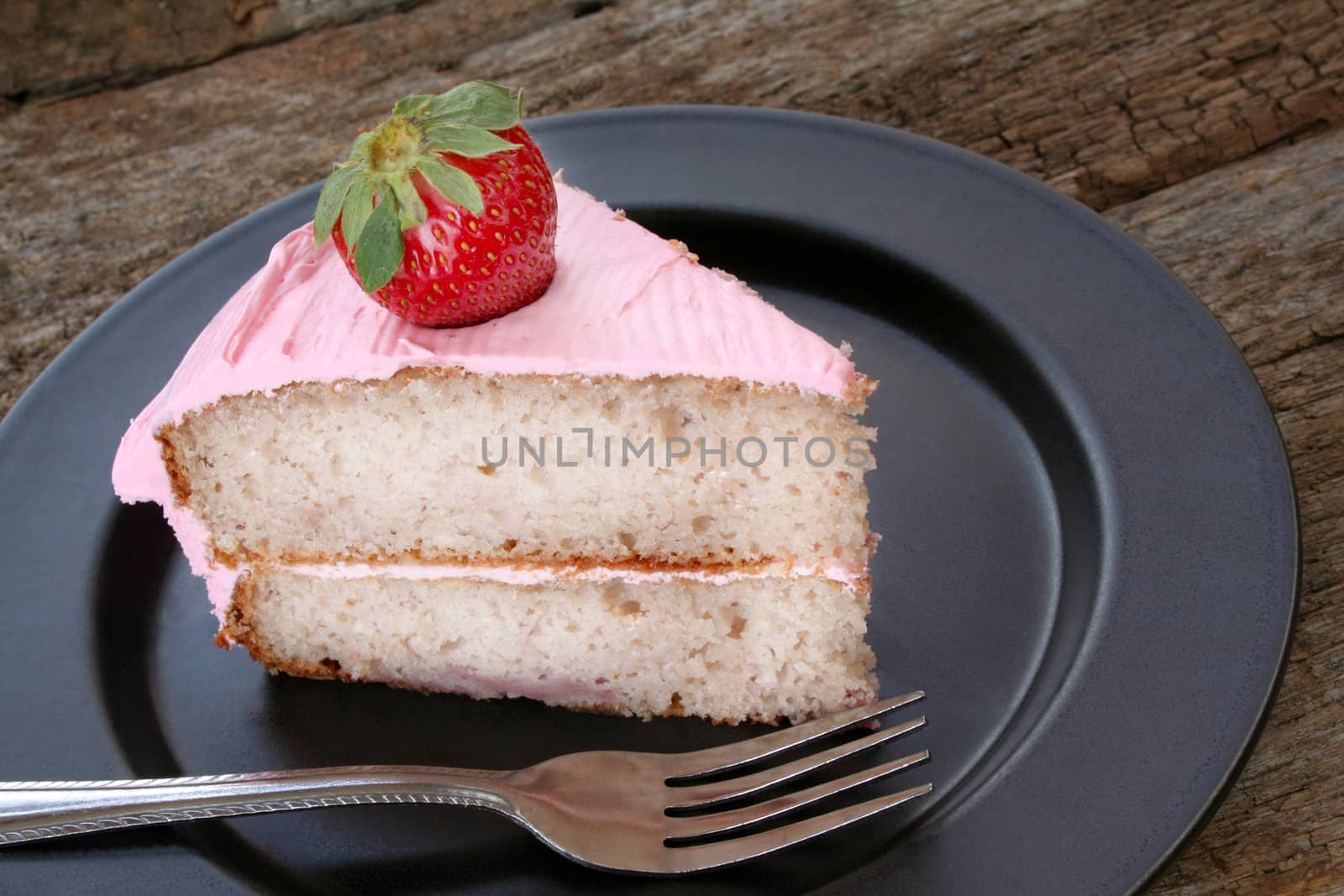 Strawberry cake with strawberry icing and garnished with a fresh strawberry.