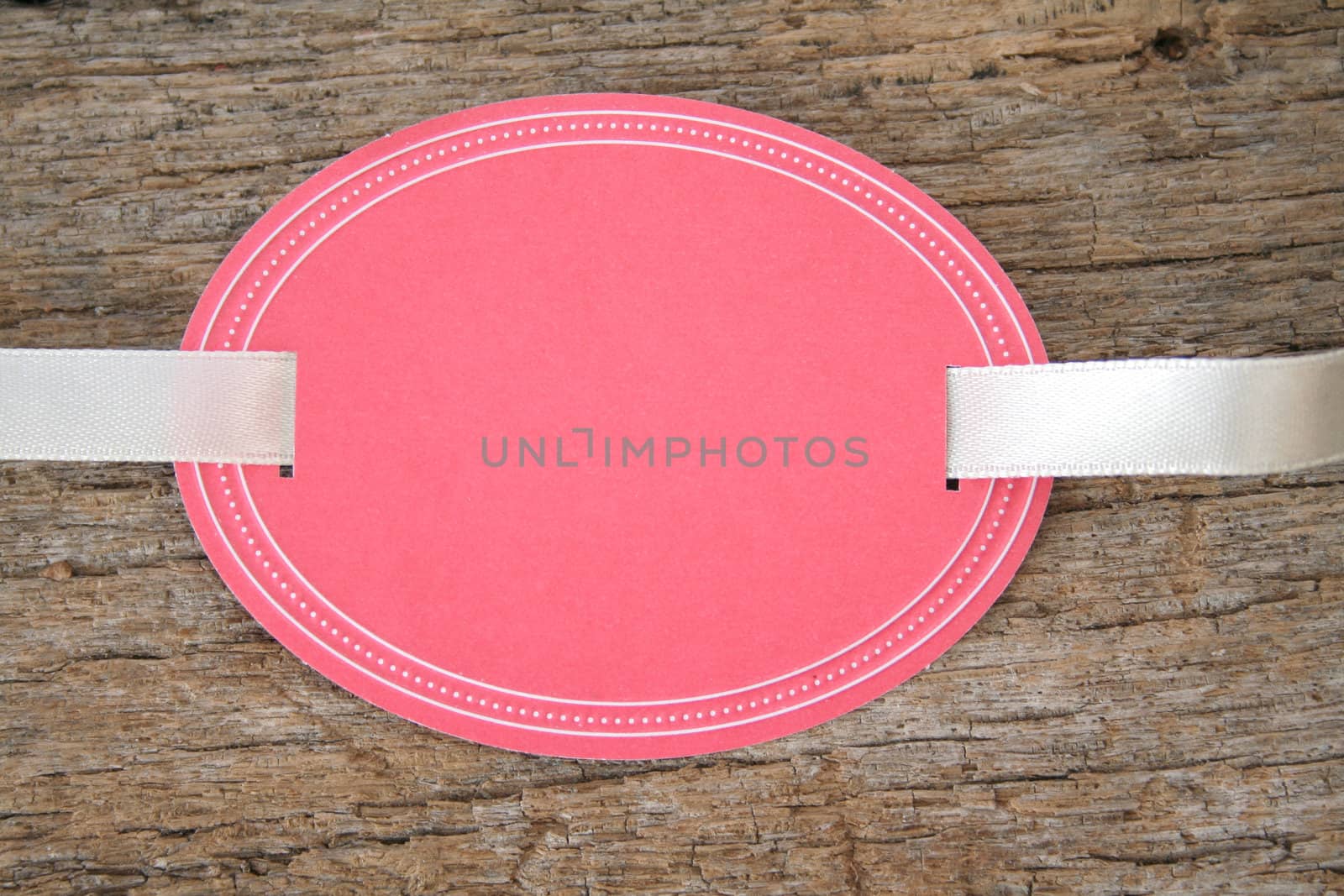 Blank oval shaped tag with ribbon on an old piece of wood.