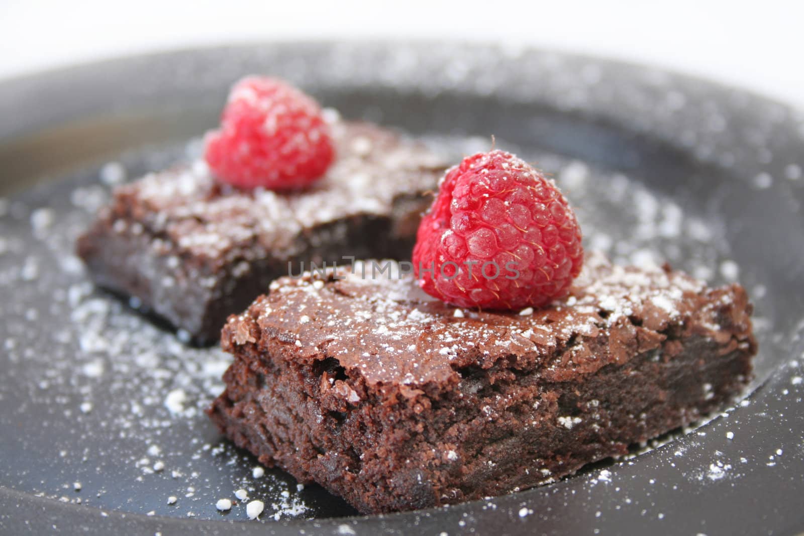 Two brownies with powder sugar and a raspberry.