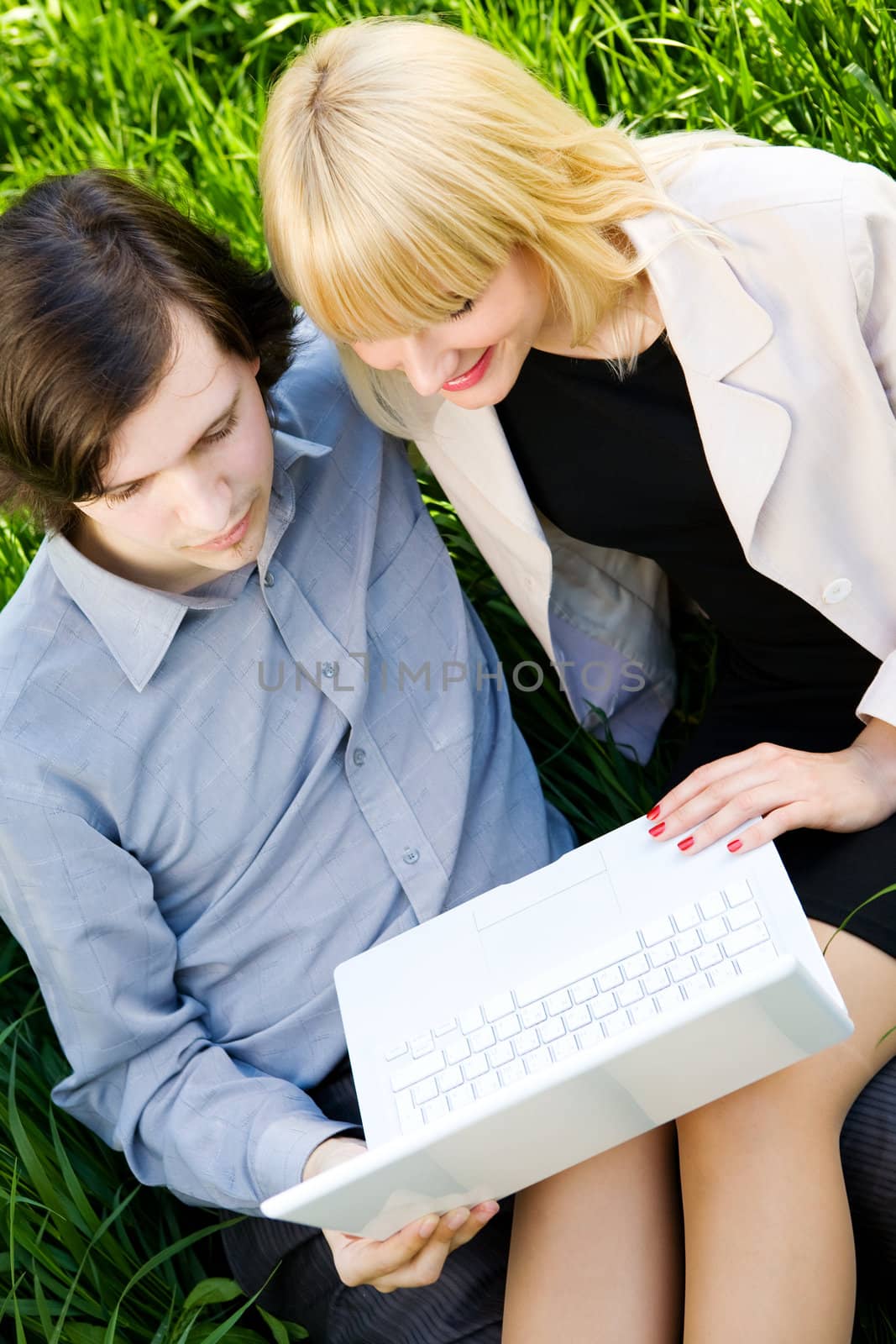 boy and girl sit on the grass and look in laptop