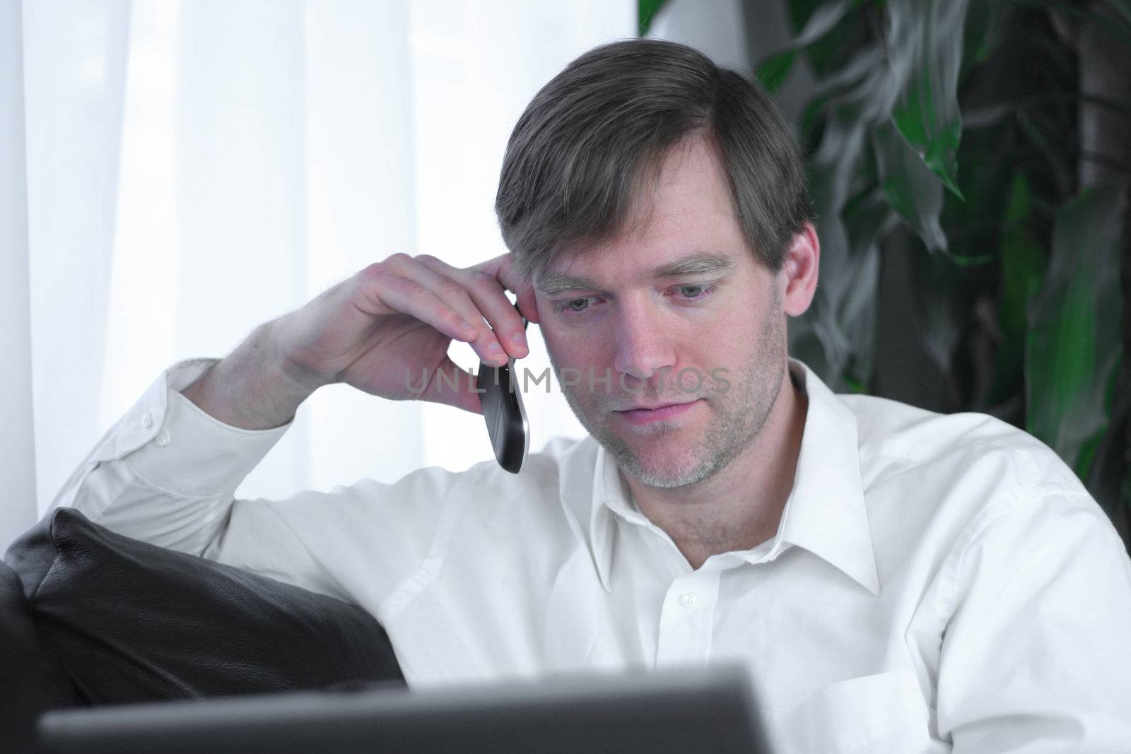 Handsome businessman working on laptop and using cell phone in casual attire.