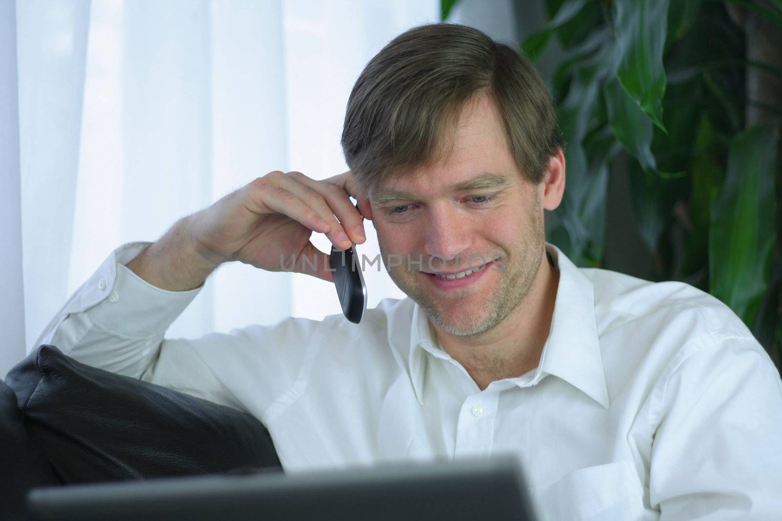 Handsome businessman working on laptop and using cell phone in casual attire.