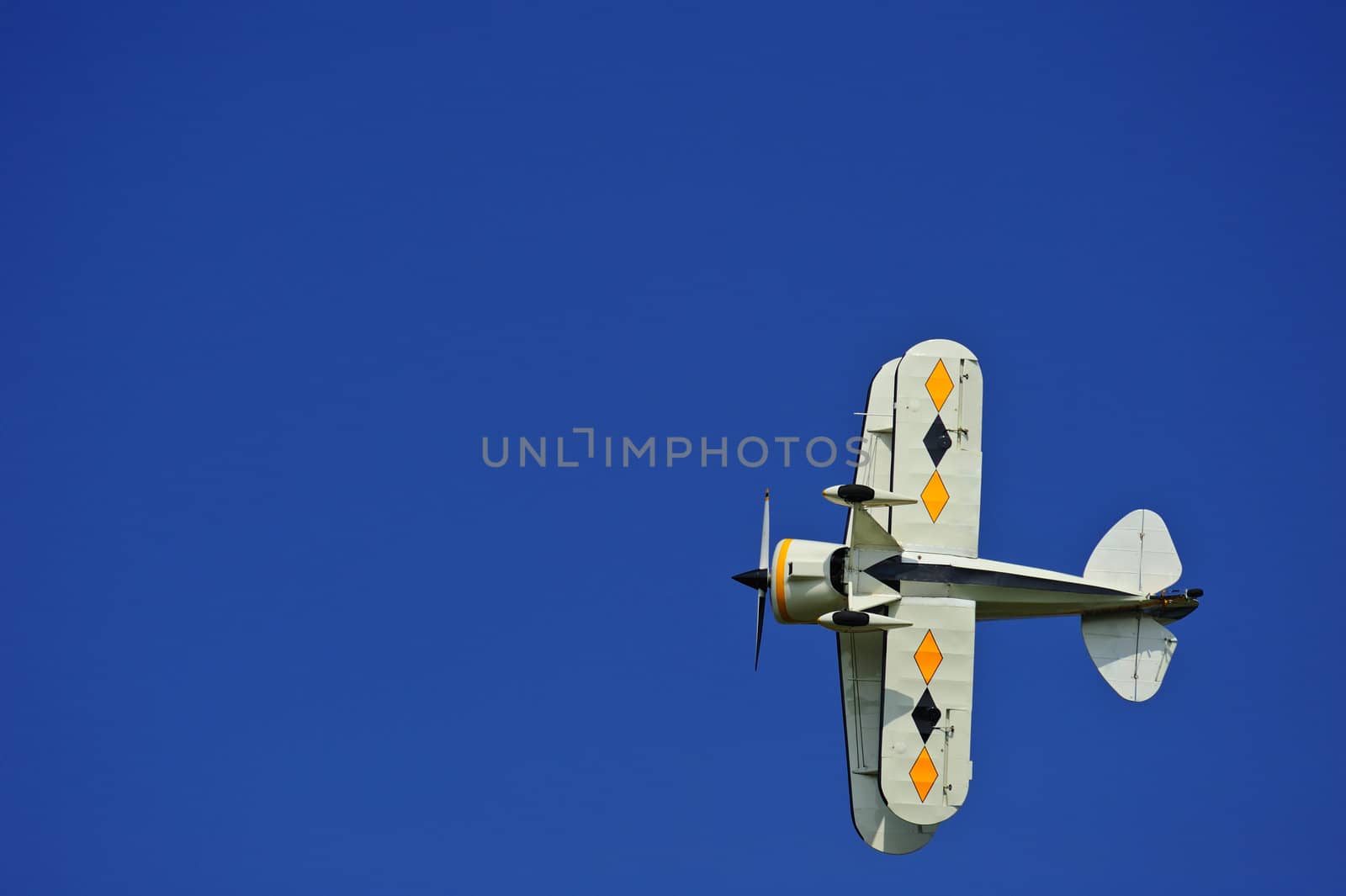 An aerobatic biplane flying directly overhead. Space for text in the sky.