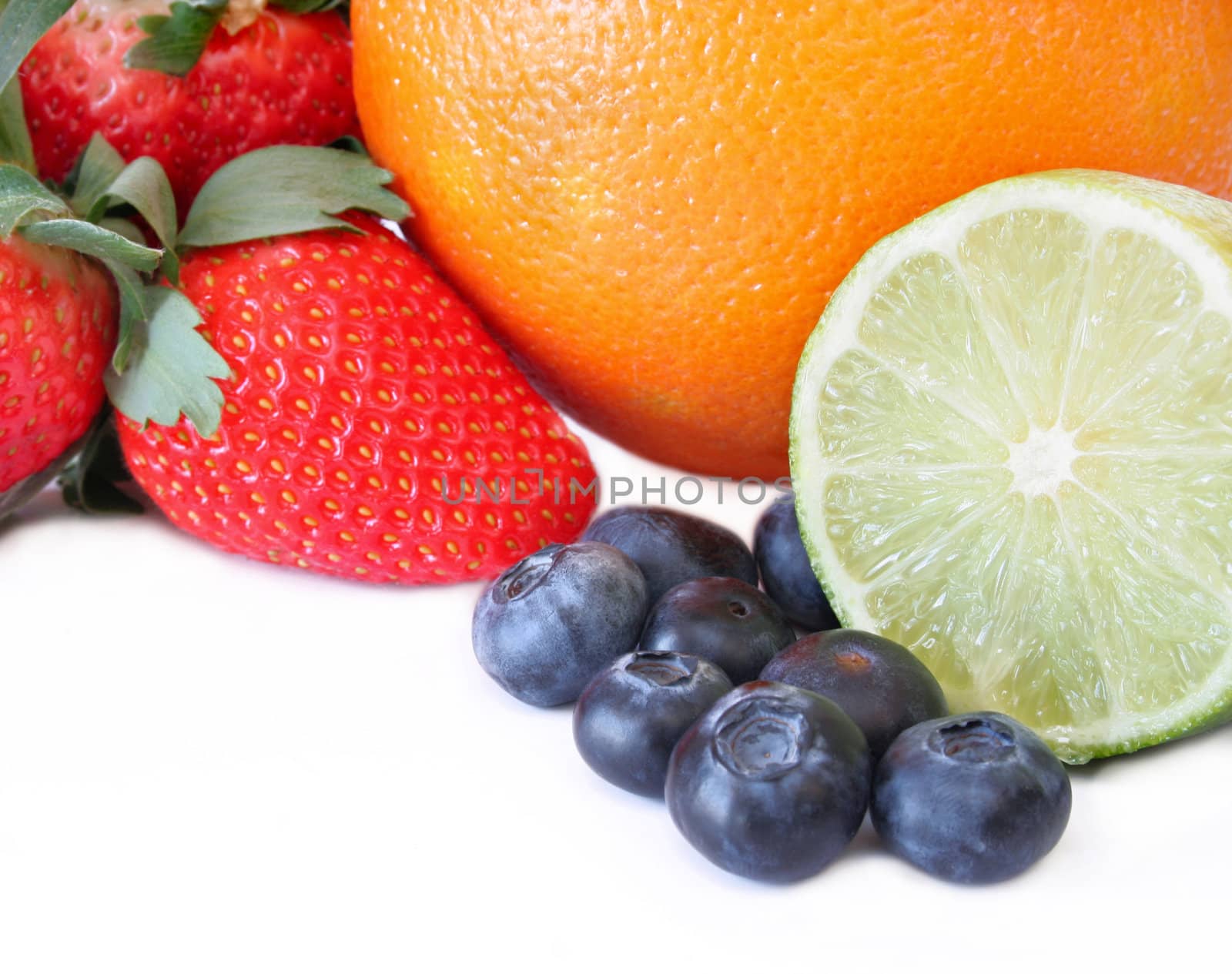 Strawberry, blueberries, Lime, and an orange all on a white background with copy space.