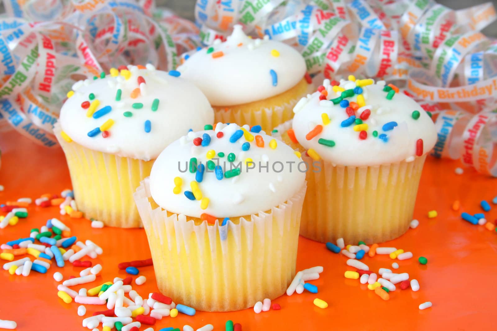 Cupcakes with sprinkles sitting on an orange background.