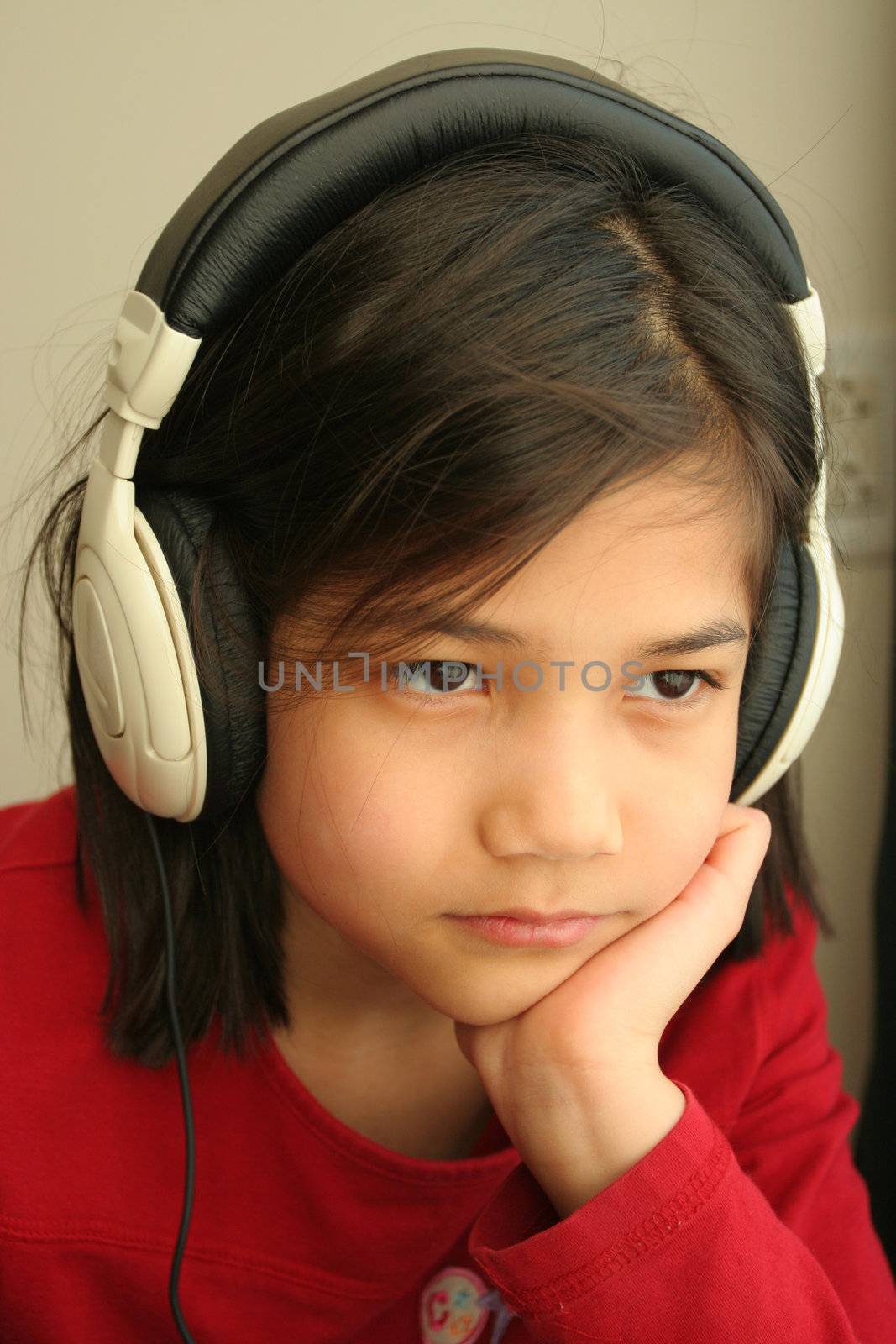 Child with sad expression listening to music on the headphones. Part asian, scandinavian descent.