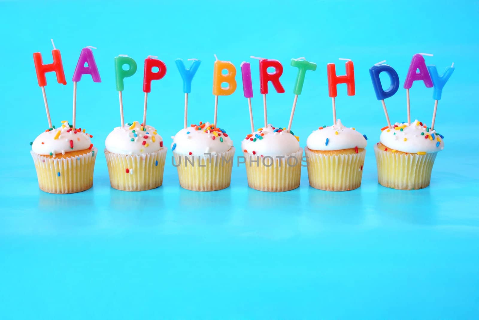Cupcakes with Happy Birthday Candles on them against a blue background and plenty of room for copy space.