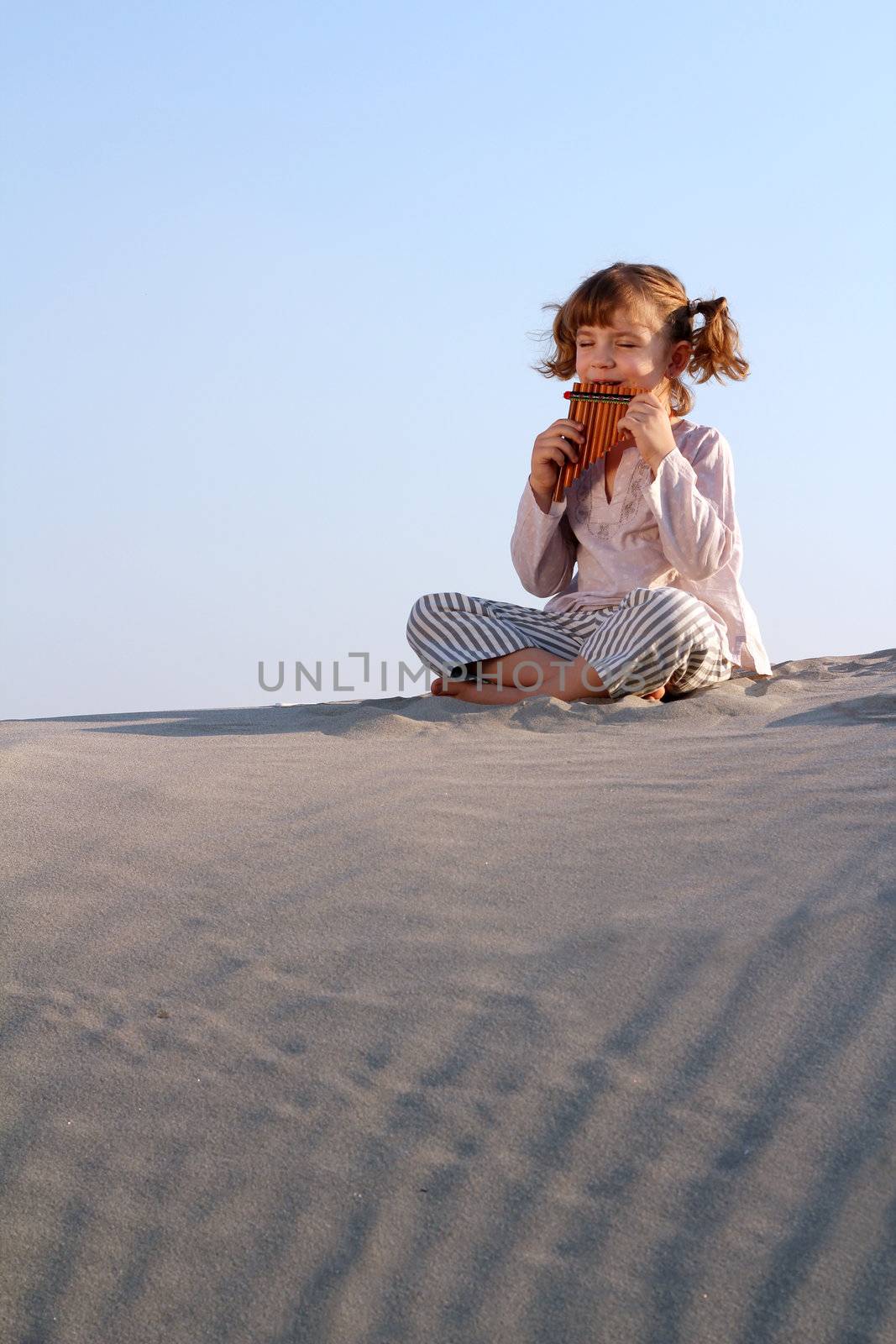 happy little girl play pan pipe in desert by goce