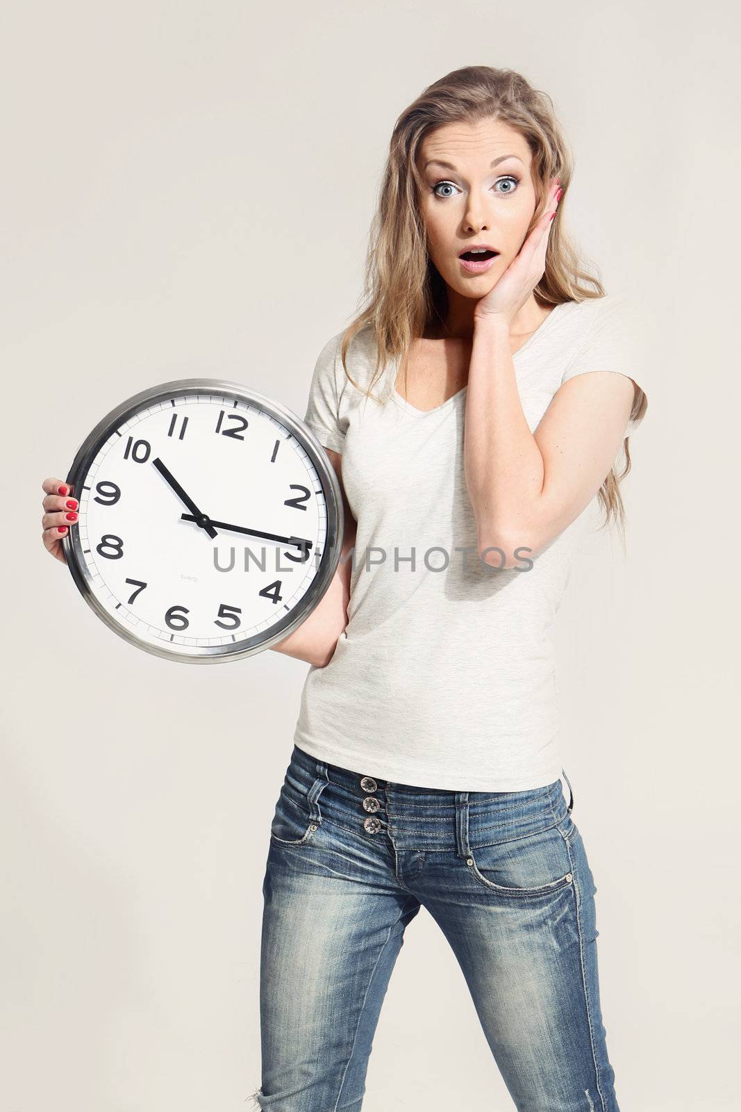 Surprised attractive young woman holding big clock