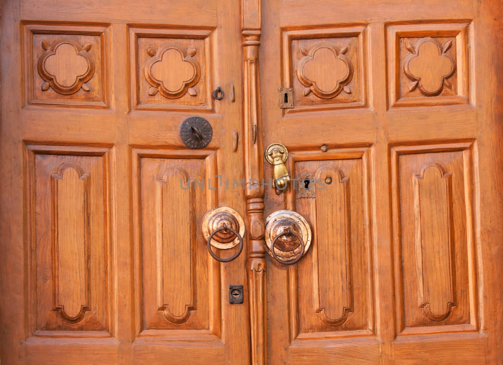 An old-fashioned wooden door with a knocker in the shape of a hand and several keyholes.