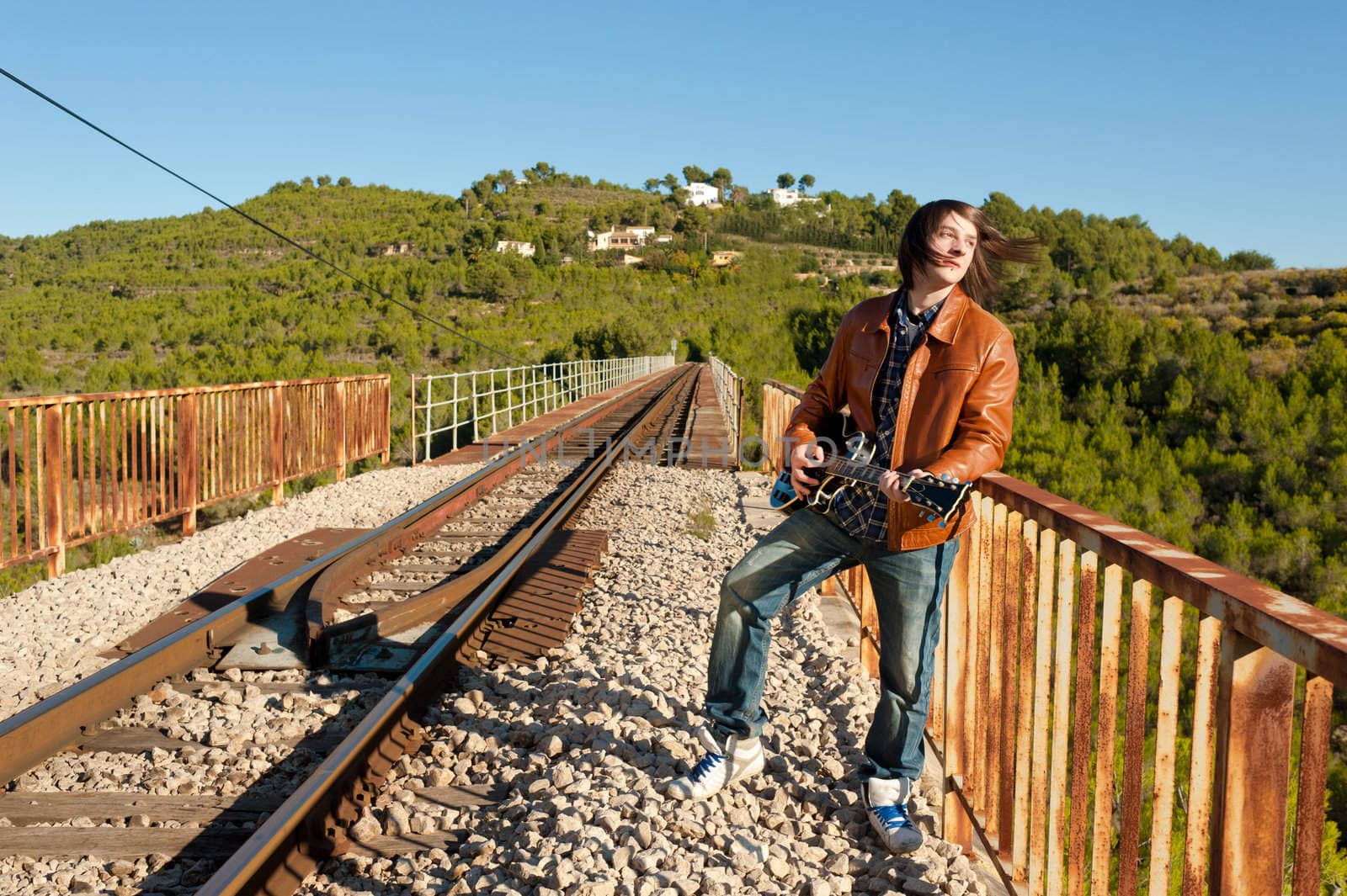 Young guitarist playing on a rusty railway bridge