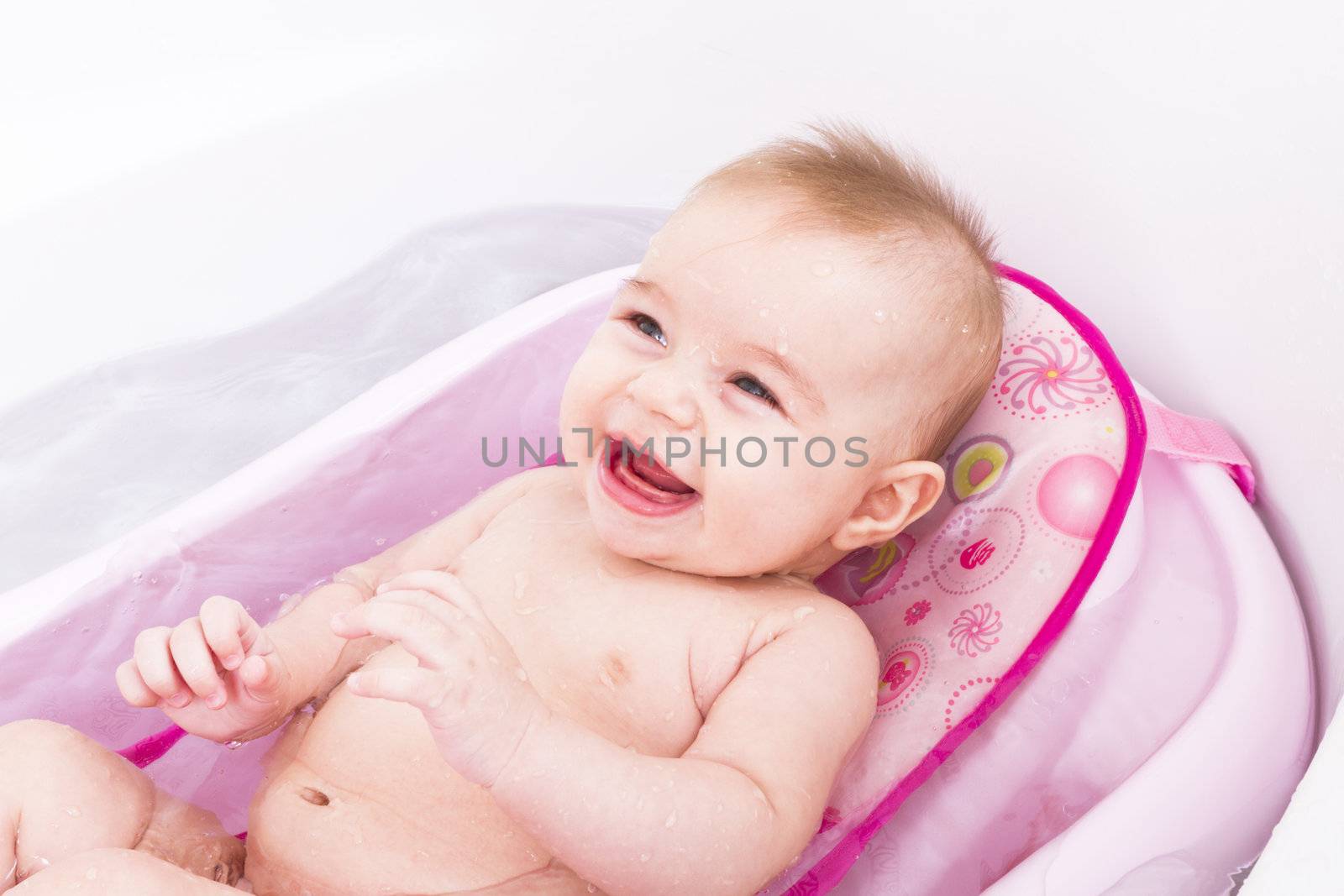 Pretty smiley baby girl is having a bath in her bathtub.