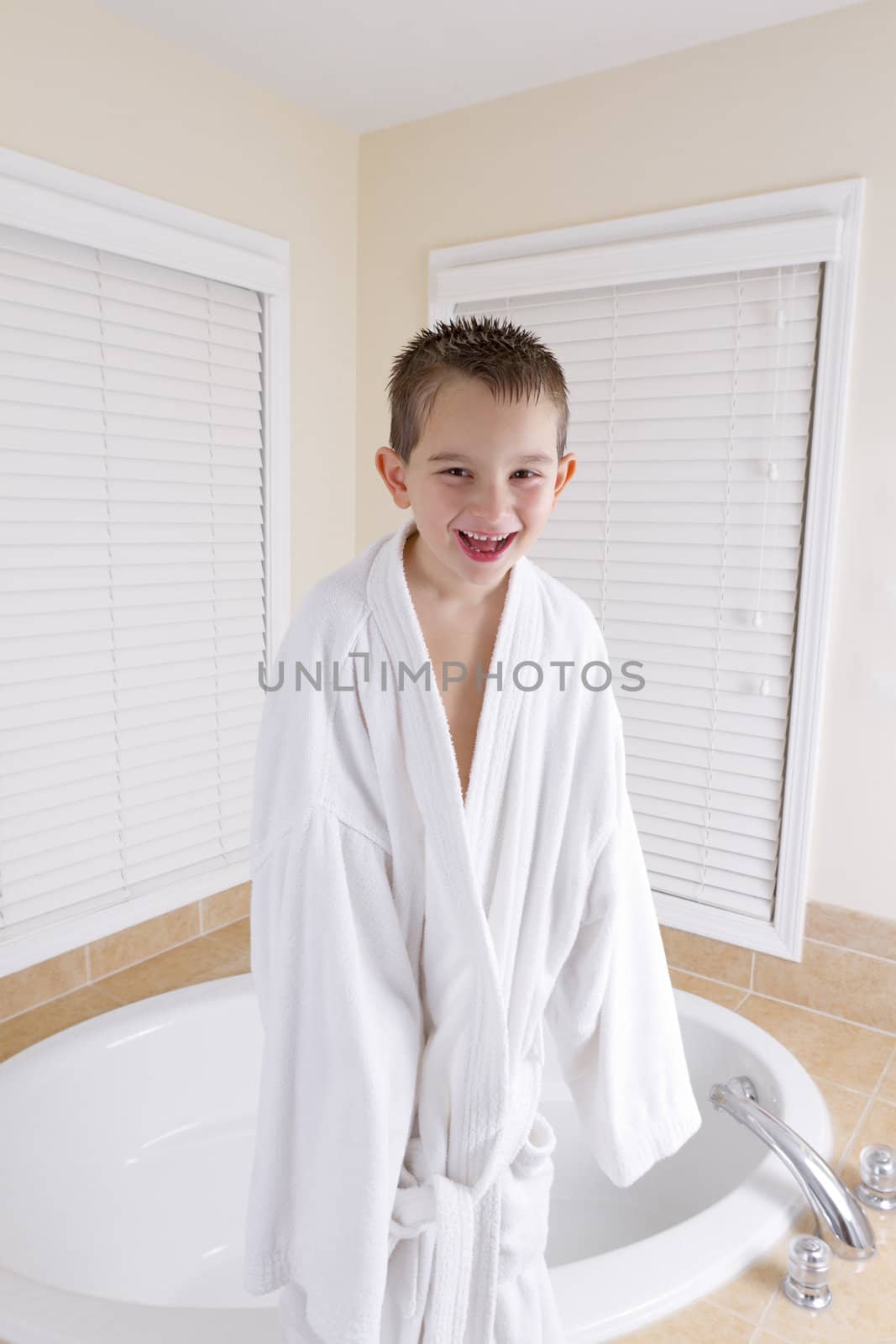Mischievously smiling kid is wearing dad's bathrobe.