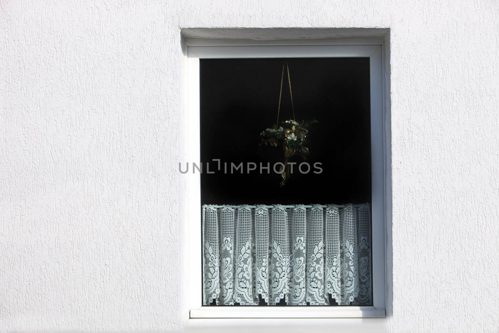 Outside view of a window in a white exterior wall of a house with a decorative net curtain on the lower half