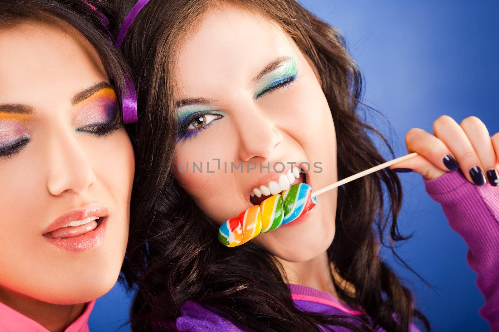 Close-up of two beautiful girls - one of them giving a blink and biting lollipop