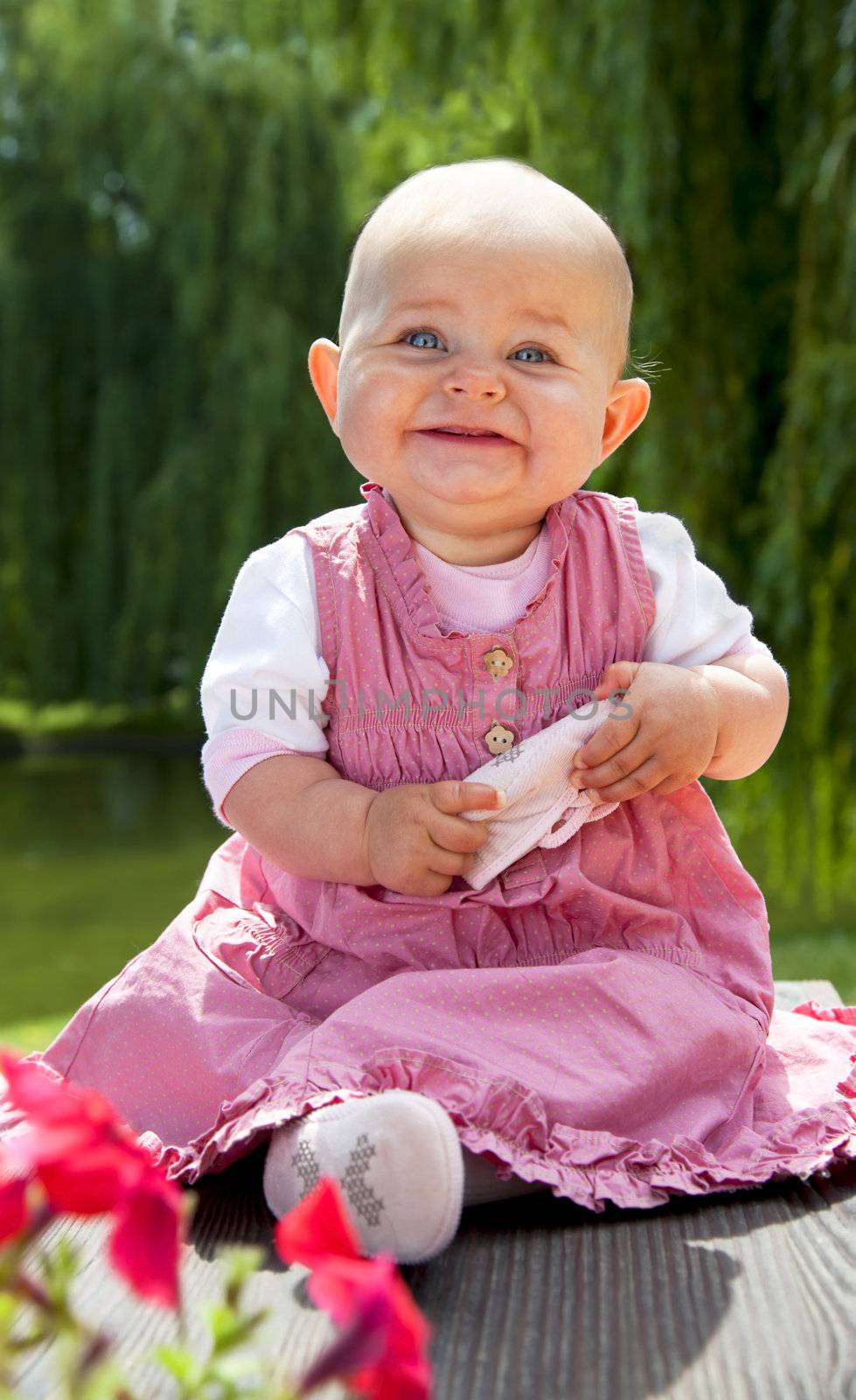 Sweet baby girl with blue eyes sitting in the park and smiling