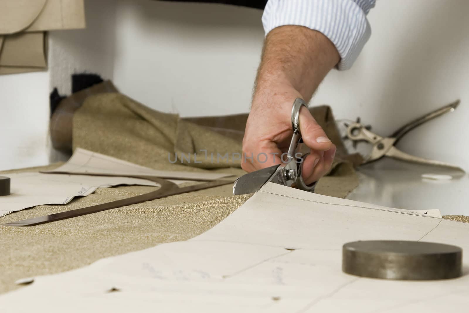 Tailor working at studio cutting fabric, detail of hand with scissors