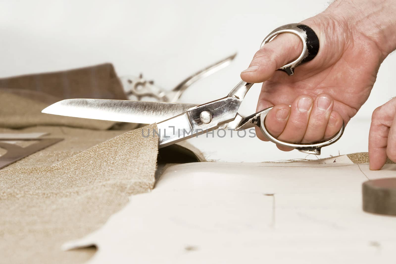 Tailor working at studio cutting fabric, detail of hand with scissors