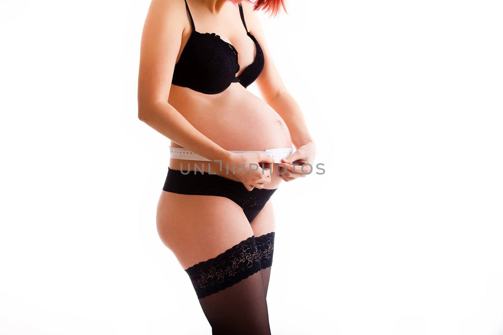 Pregnant woman wearing lingerie and measuring her belly