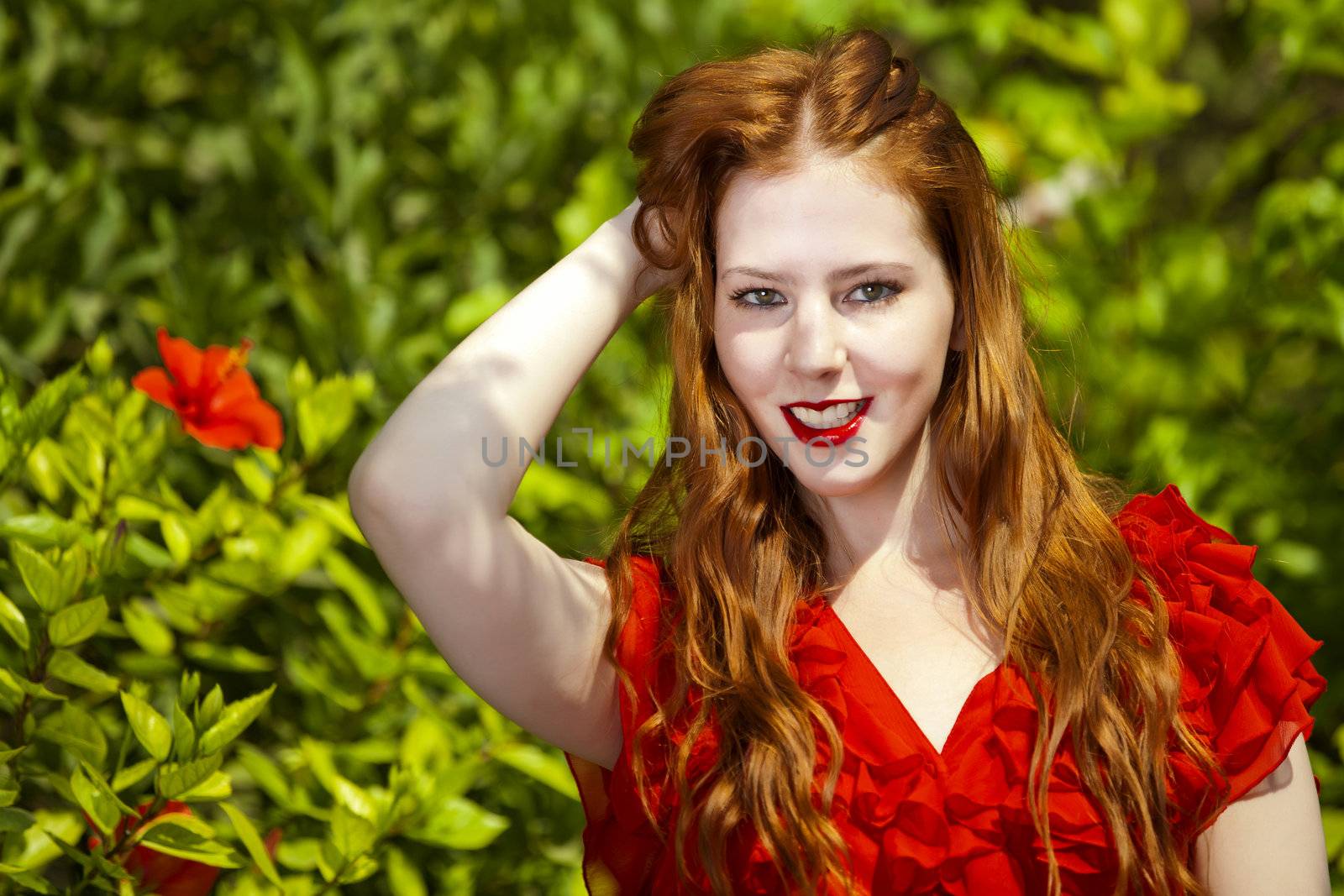 Beautiful model with white skin wearing a red dress with green foliage in background