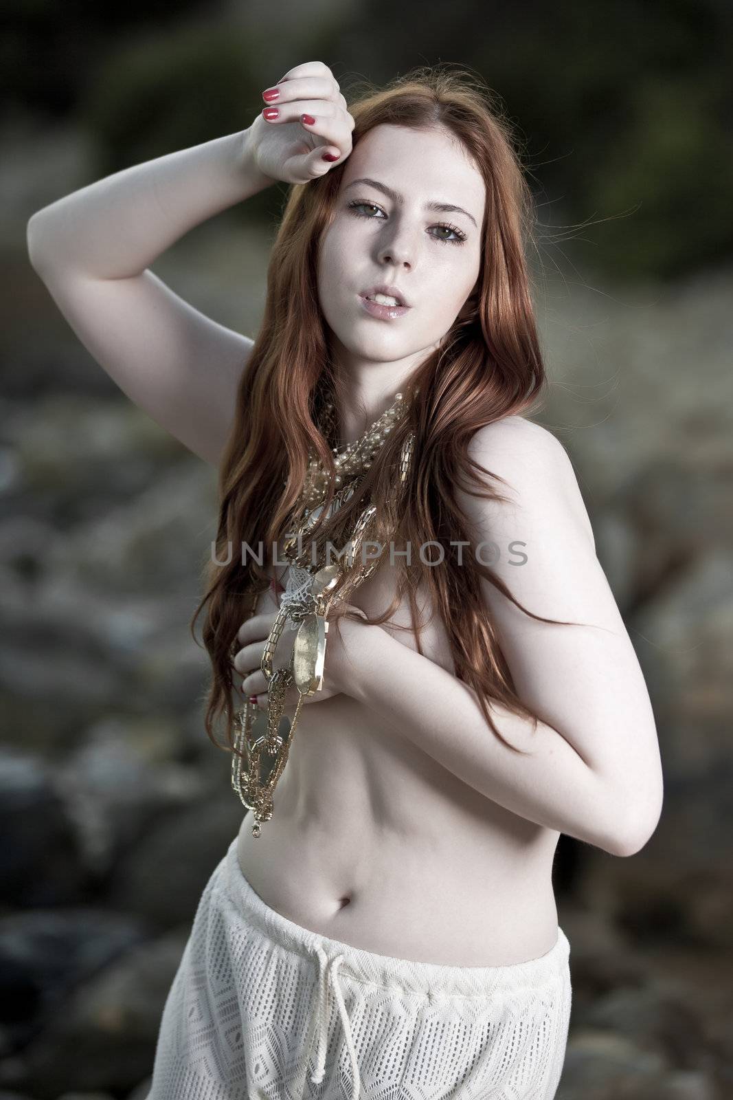 A semi-nude woman with beautiful white skin and long red hair outdoors on a beach