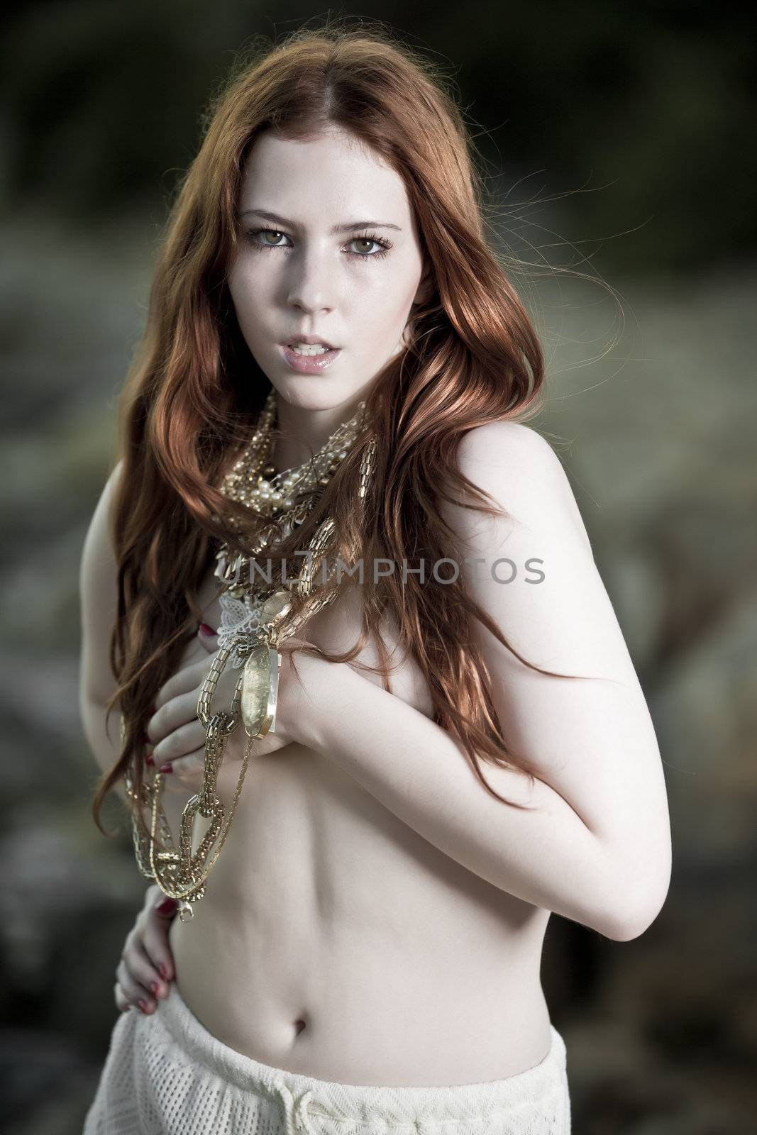 A semi-nude woman with beautiful white skin and long red hair outdoors on a beach