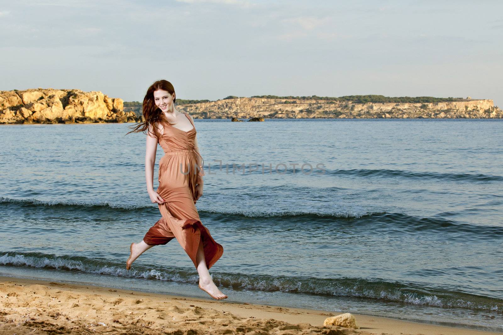 A young female model and dancer jumps and dances on a Mediterranean beach