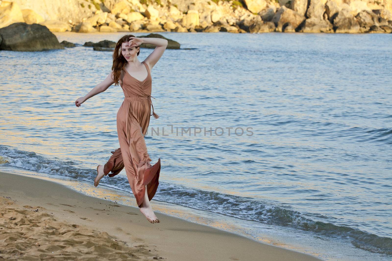 A young female model and dancer jumps and dances on a Mediterranean beach