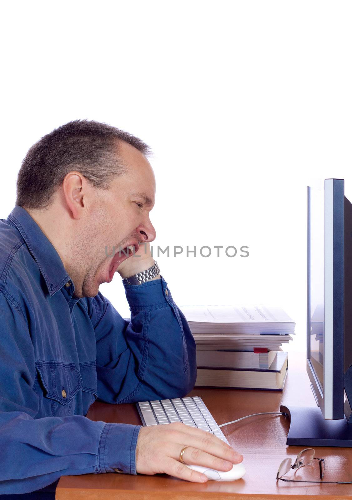 Tired man yawning at his computer keyboard