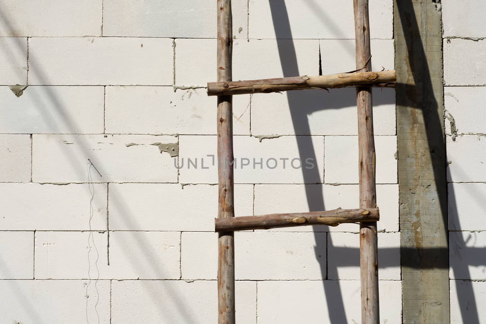 Wood ladder leaning on white brick wall being construct