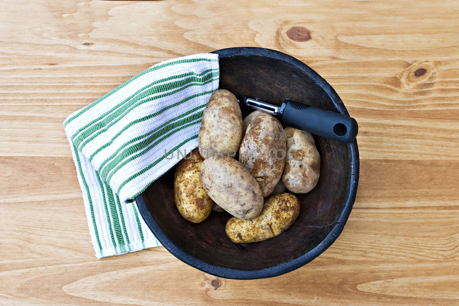 Freshly washed potatoes in a hand carved wooden bowl with kitchen towel.